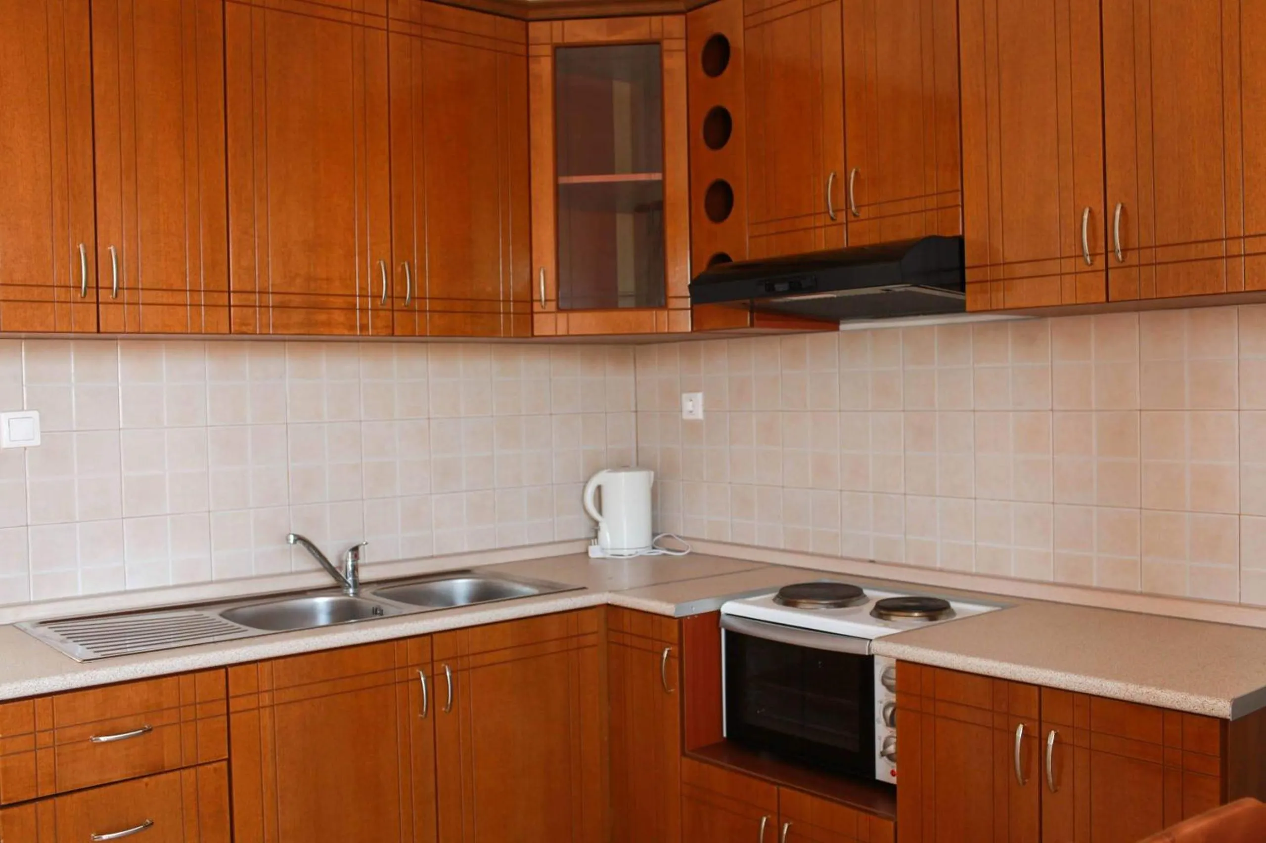 A kitchen with cherry-wood cupboards, an electric hob and oven, a white fridge and a small wooden table with two chairs
