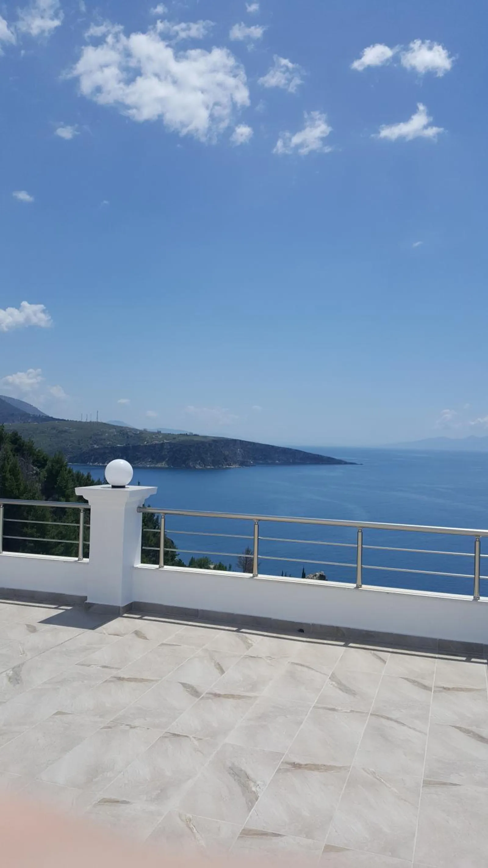 The roof terrace by day: pale tiles, a white post with a globe lamp, a stainless rail and the coast running away beyond it