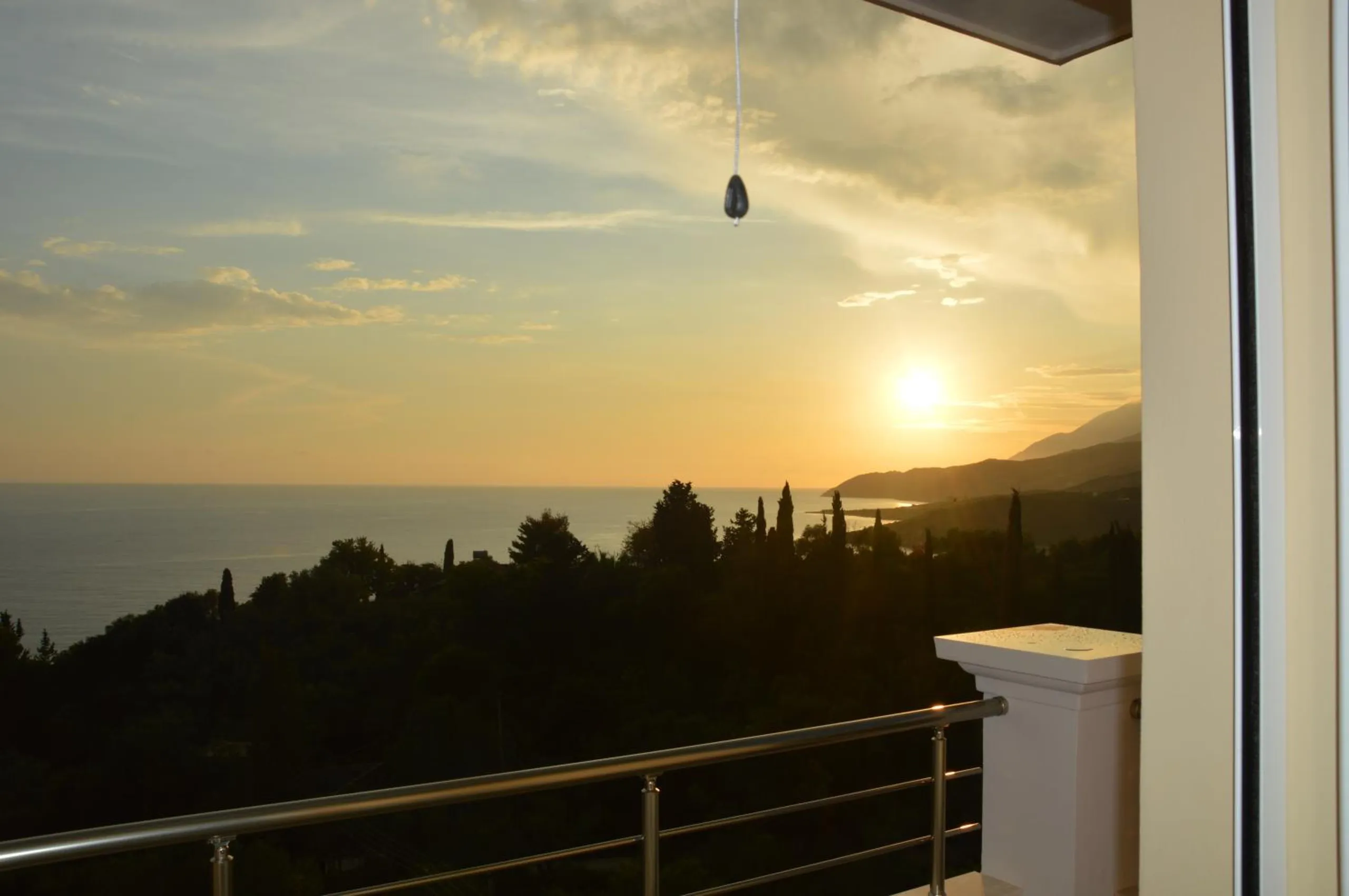 The sun setting over the sea and a long headland, seen past a balcony rail and a white post