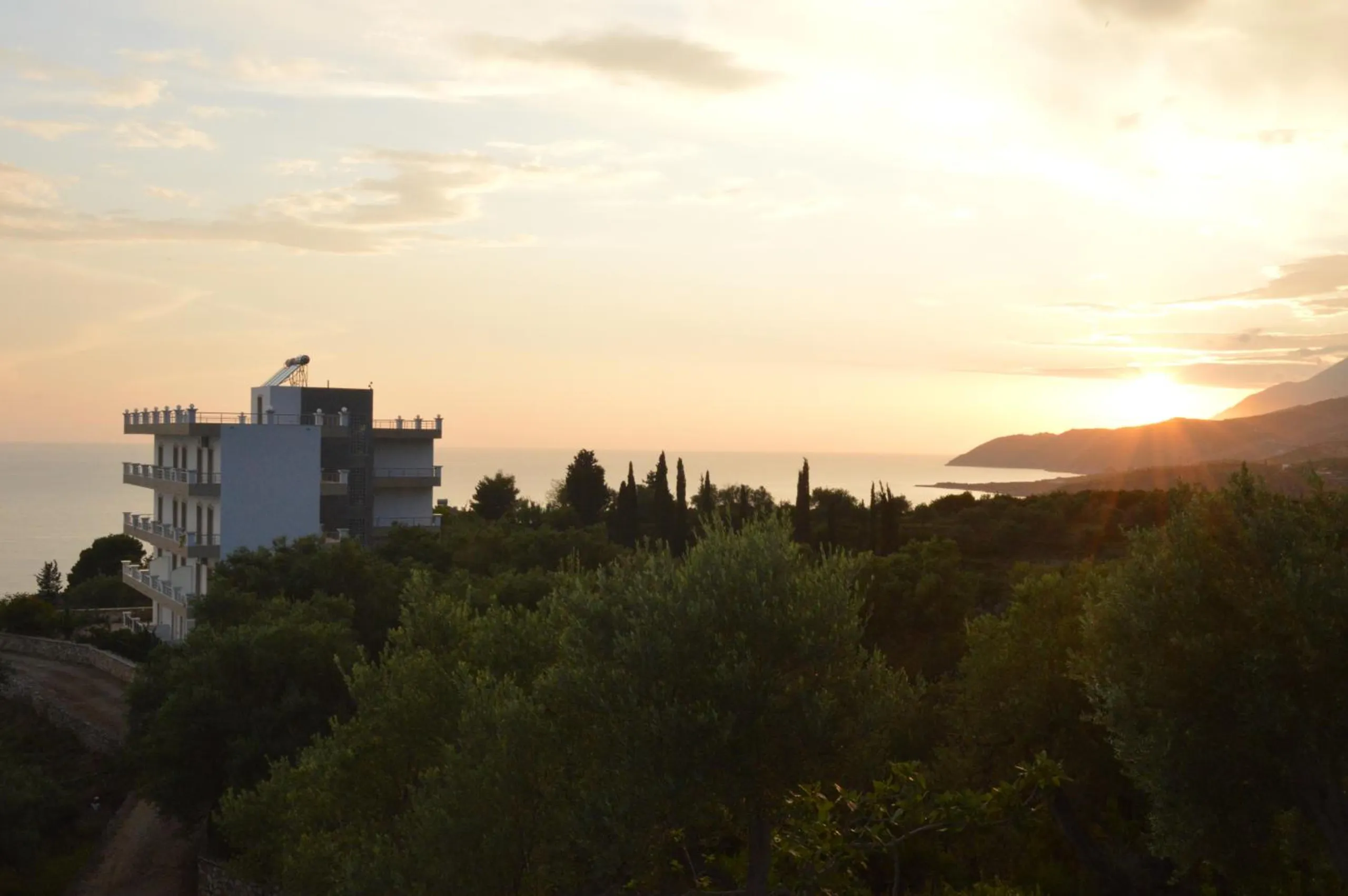 The house among the olive trees with the sun low over a headland across the bay