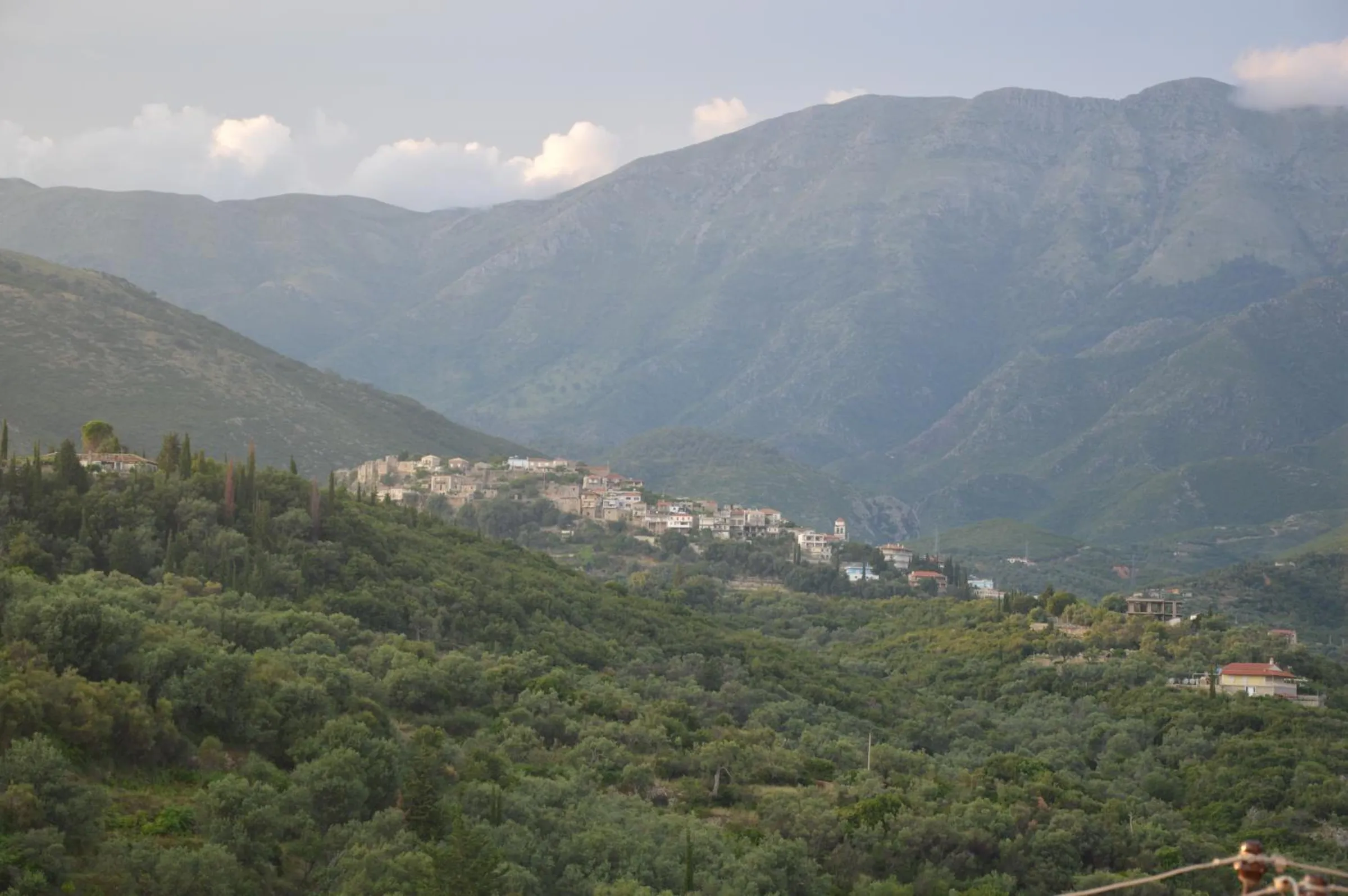 The view inland from the house: a green valley of olive groves rising to a hillside village and the mountains behind it