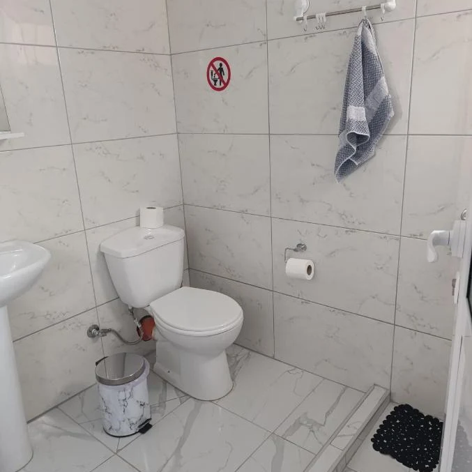 The private shower room of an apartment at Nikolari Resorts, marbled white tiles floor to ceiling, a corner shower tray and a folded grey towel on the rail