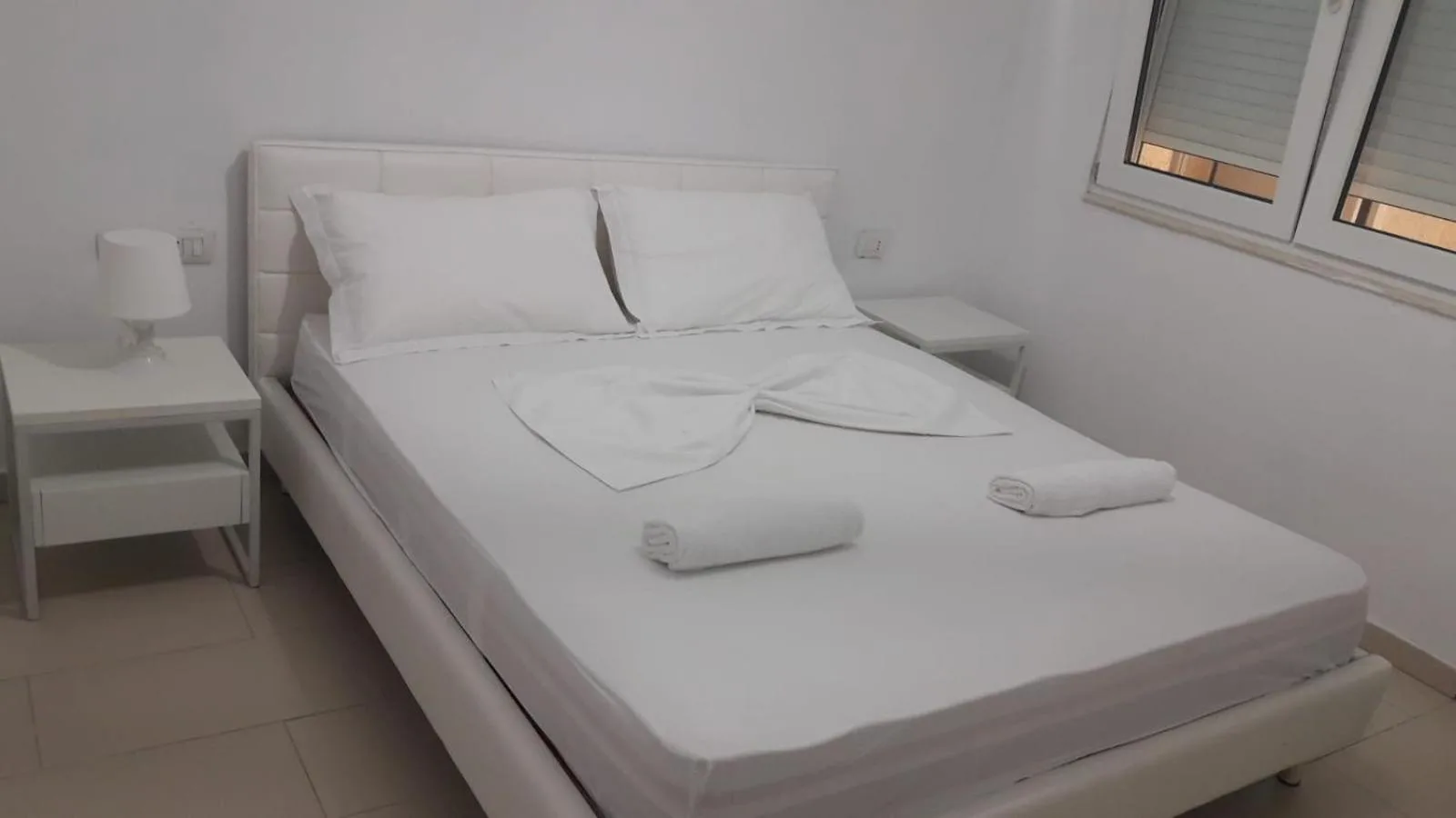 A white double bed with folded towels in a two-bedroom apartment