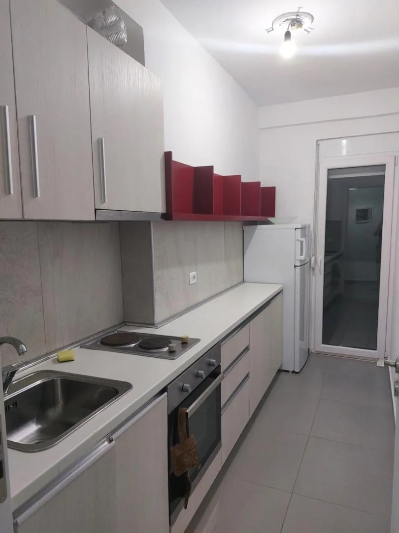 A galley kitchen with a two-ring hob, an oven, white units and a glazed door at the end