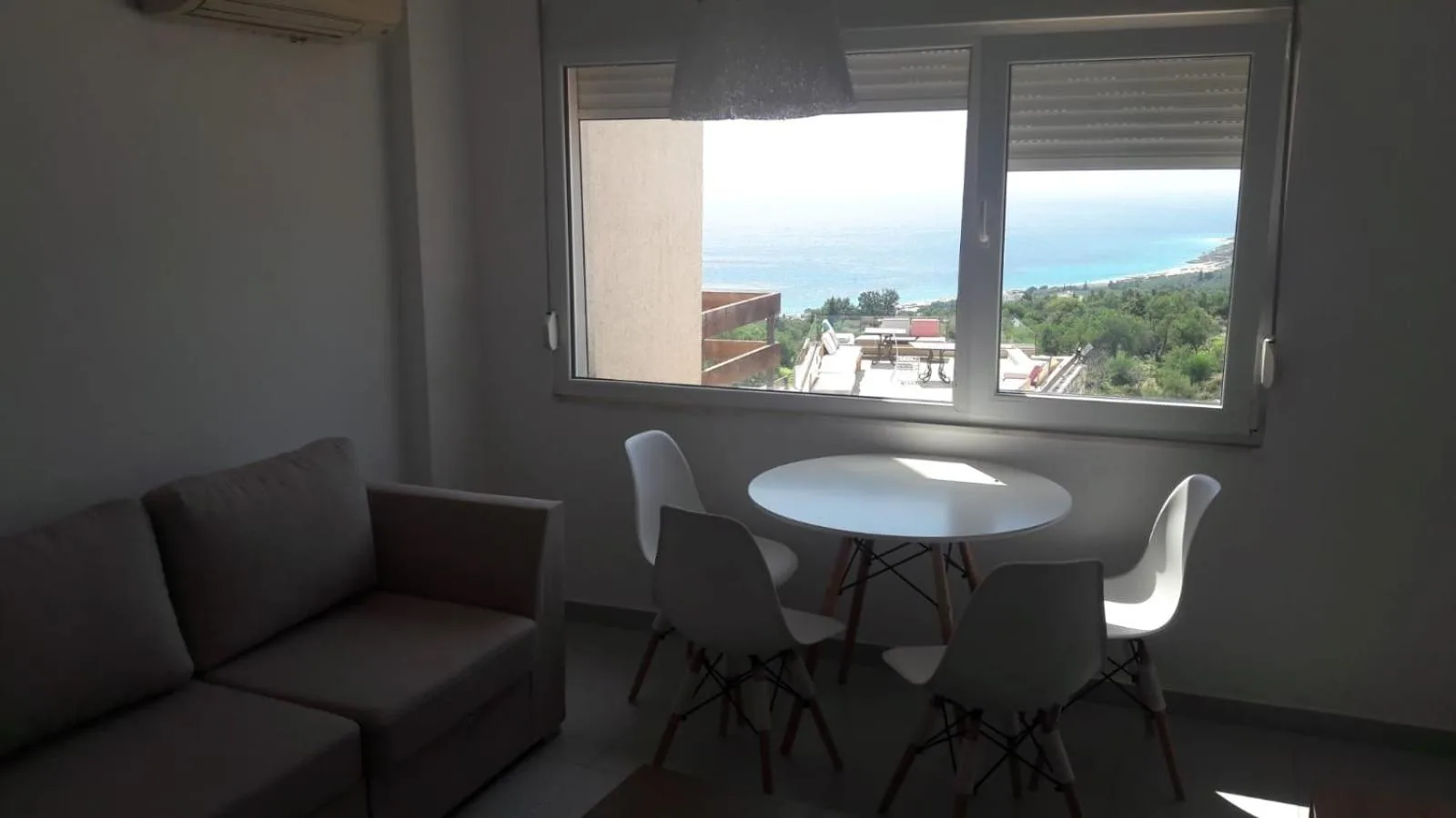 A small dining table under a window that frames the coast and the sea
