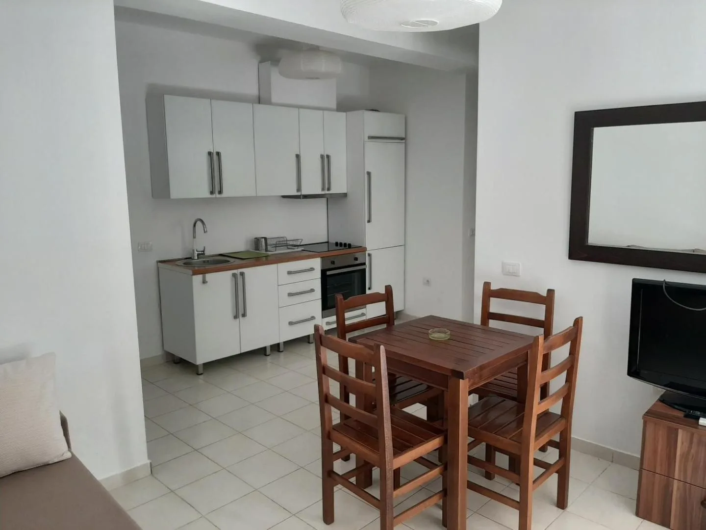A kitchen corner with white units, an oven and a wooden table with four chairs
