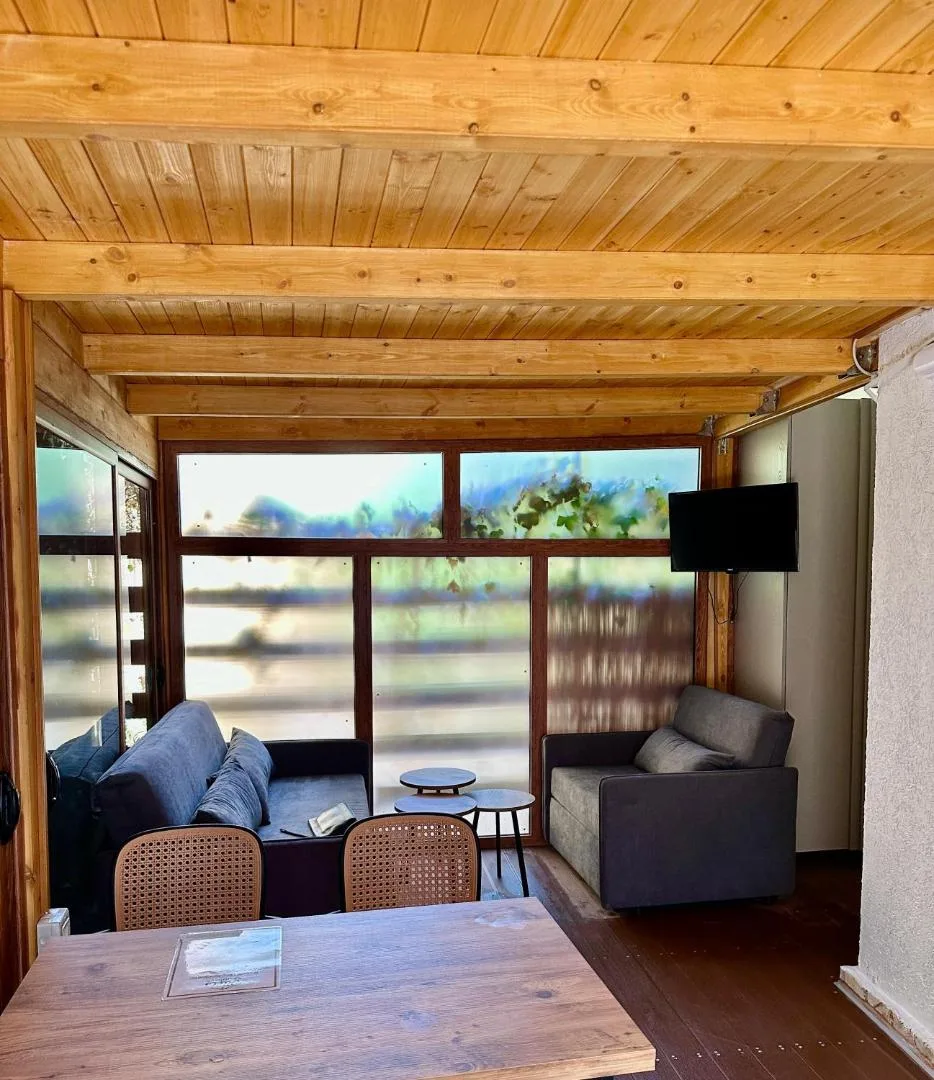 A living room under a timber ceiling with blue sofas and a wide window onto the trees