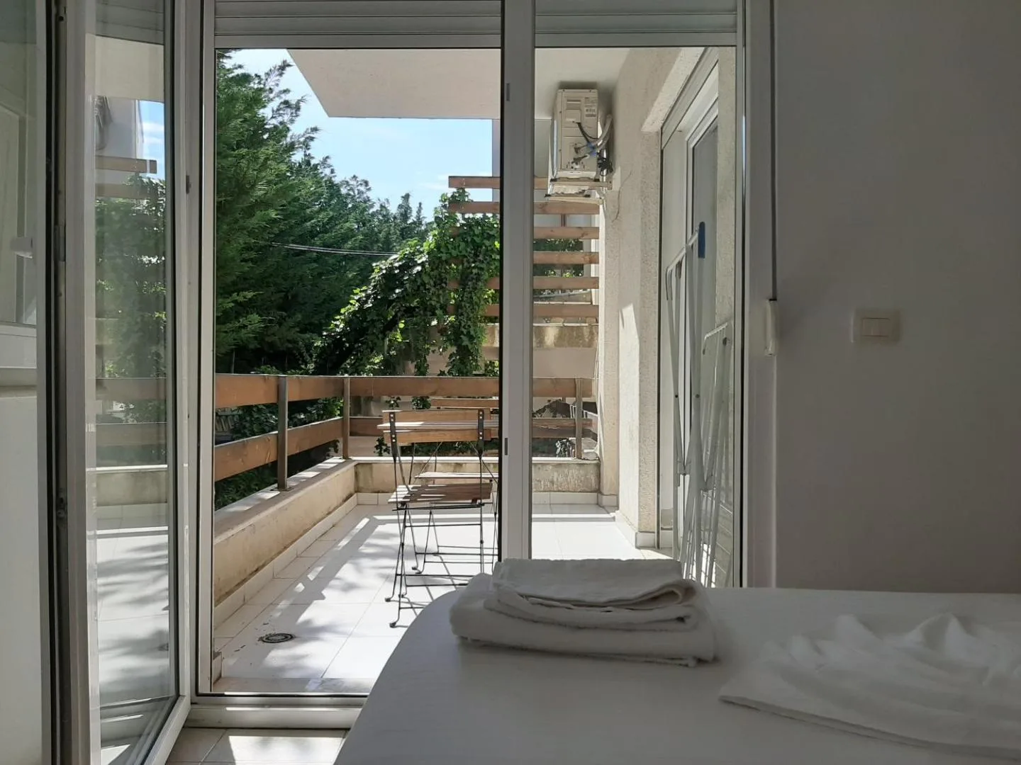 A bedroom whose glass doors open onto a terrace with a timber rail and garden beyond