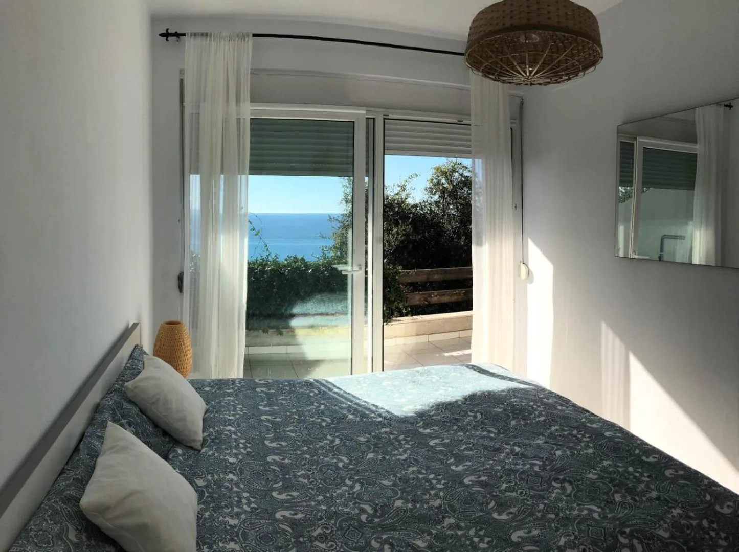 A double bed facing glass doors that open to a terrace and the sea