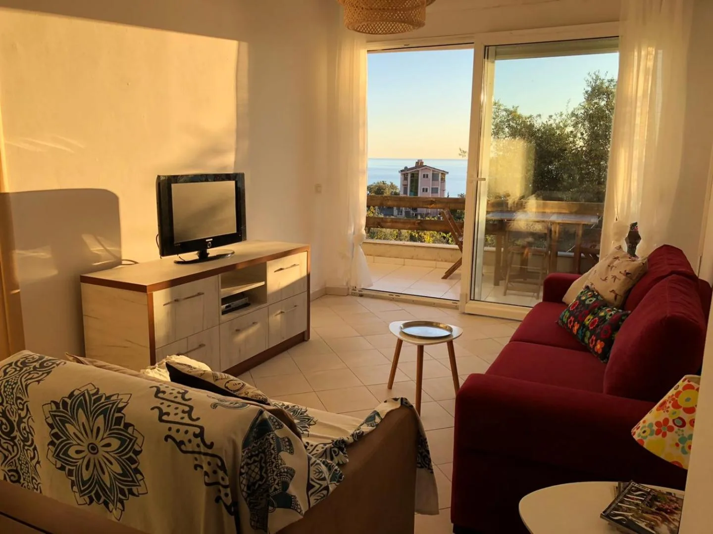 A sunlit living room with a red sofa and a glass door onto the terrace