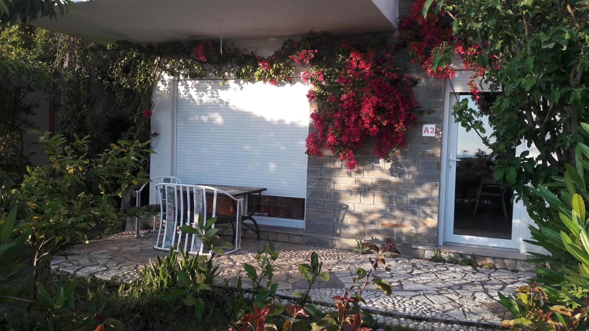 A ground-floor patio of grey stone cladding and white walls, with crimson bougainvillea over the door and a small table set outside