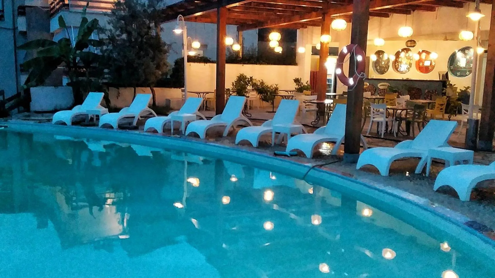 The curved pool lit at dusk, white loungers along its edge and the timber pool bar strung with lights