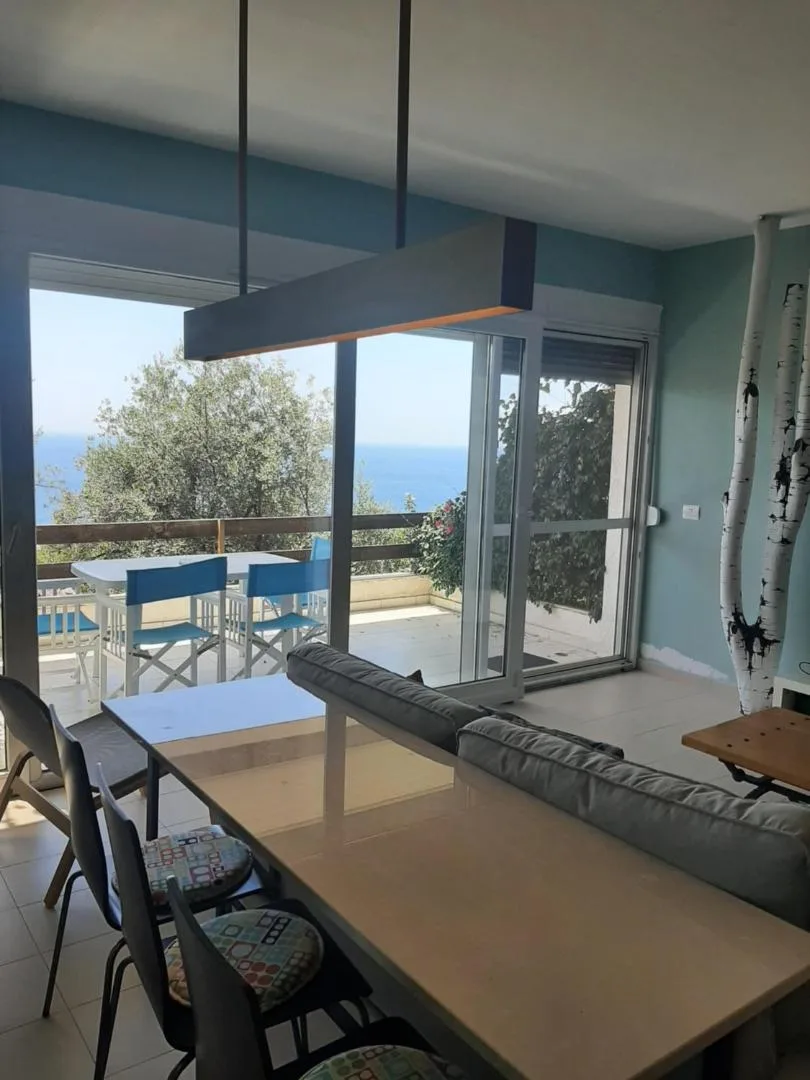 An open-plan living and dining room with a grey sofa and full-height glass doors onto the terrace and the sea