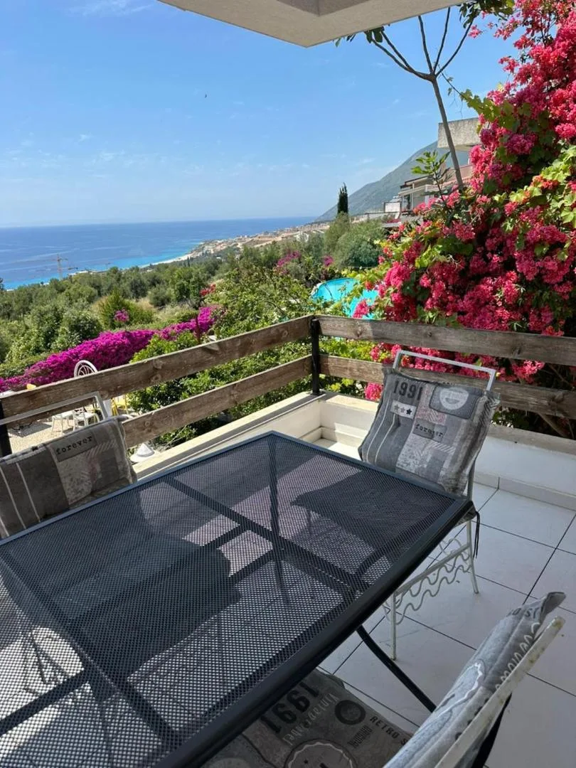 A balcony table under bougainvillea with the coast and the sea below