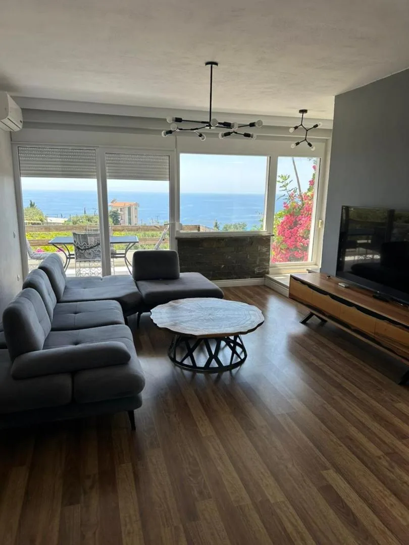 A villa living room with grey sofas, a round table and wide windows onto the sea
