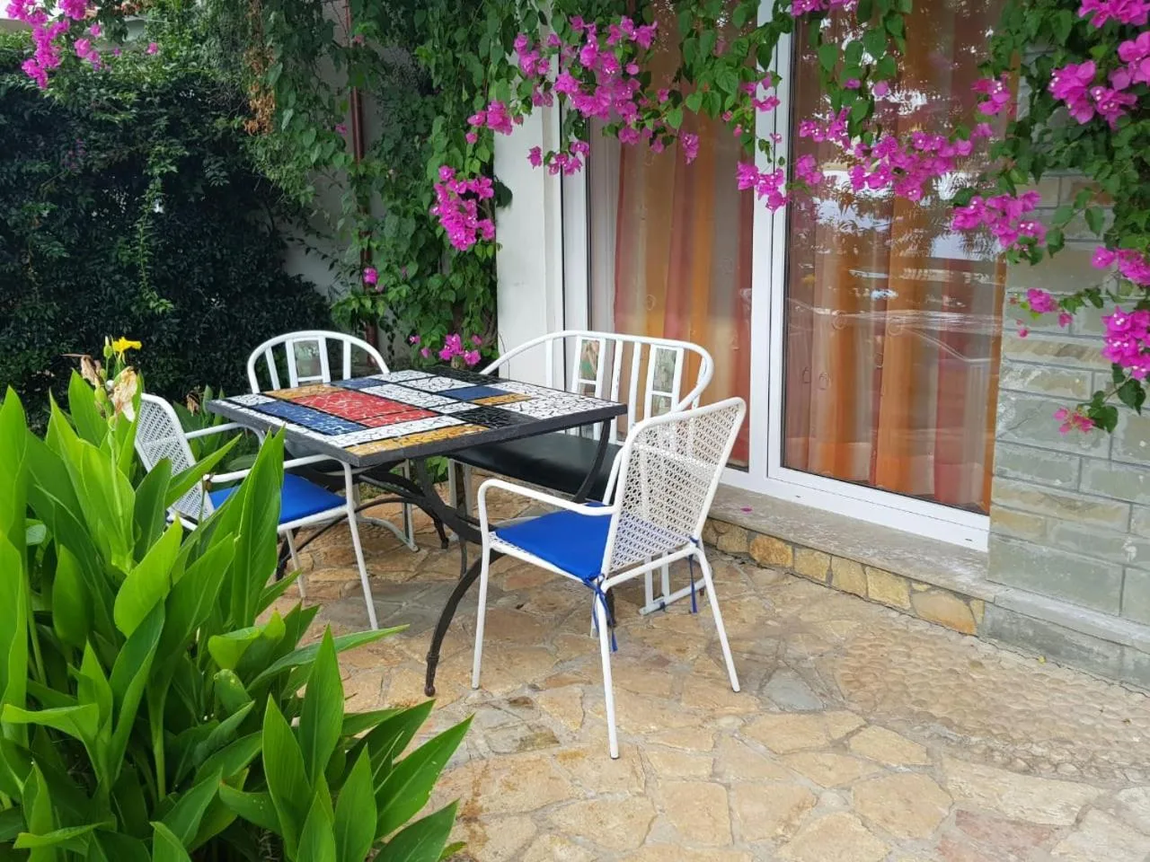A villa's stone-paved terrace with a table and white chairs under magenta bougainvillea
