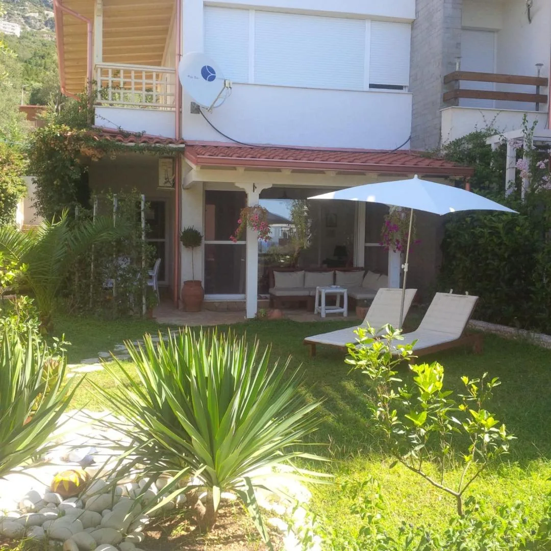 A lawn with two sun loungers and a white umbrella in front of a villa's covered porch