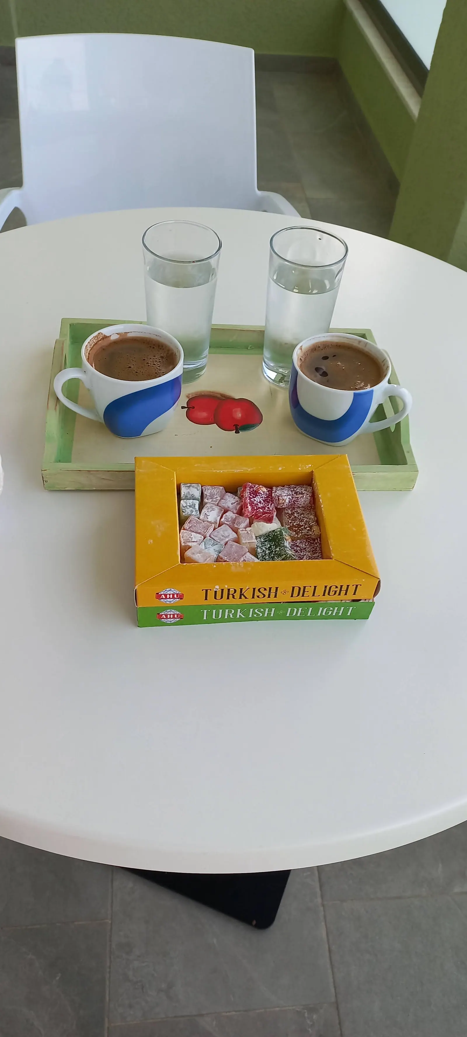 Two cups of coffee and two glasses of water on a tray on a round white balcony table, with a box of Turkish delight beside them