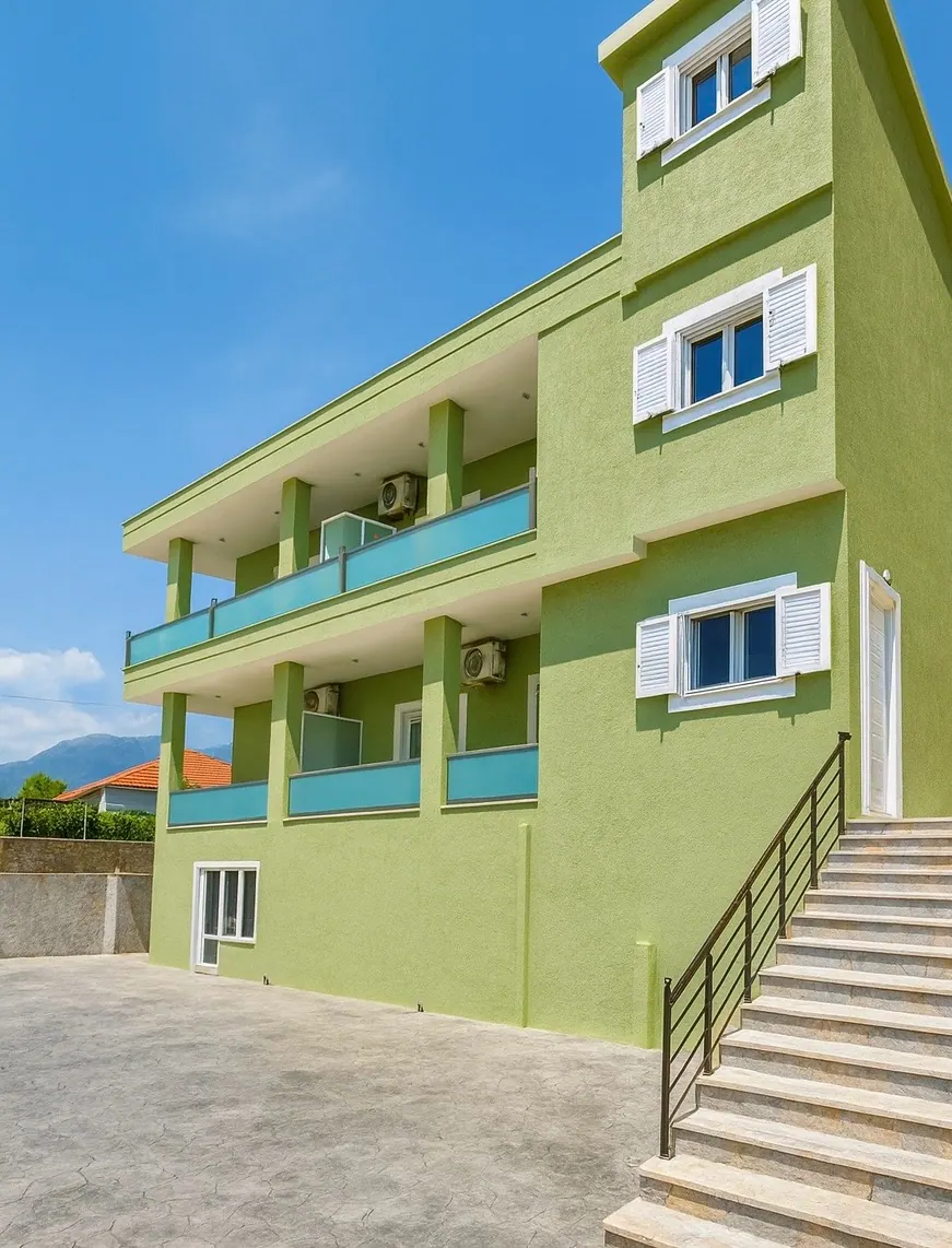 The three-storey house in lime-green render with white louvred shutters, aqua glass balconies and a stone stair climbing the outside to the upper floors