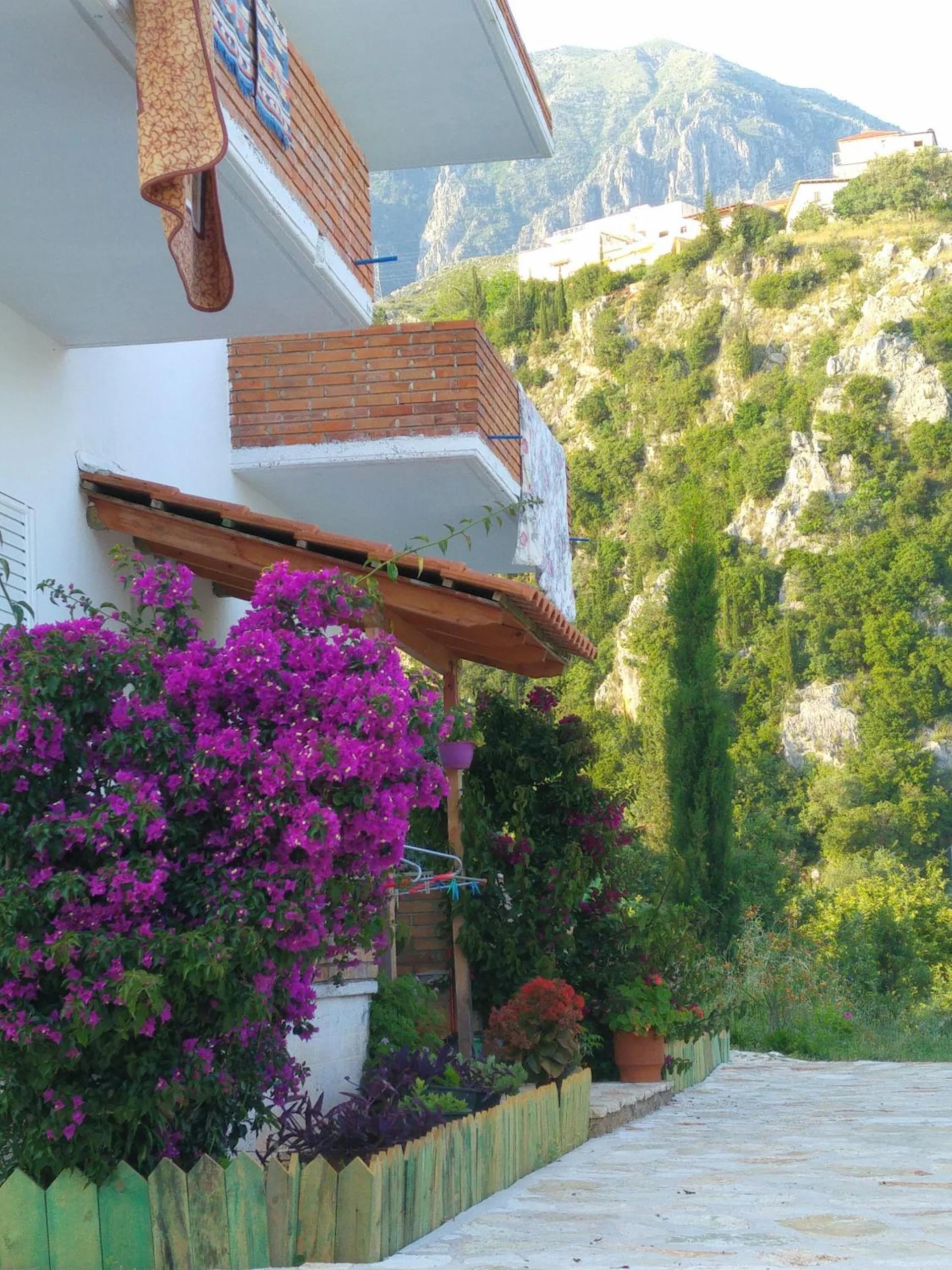 A paved path running up beside the house under a cascade of magenta bougainvillea, cliffs and green hillside behind
