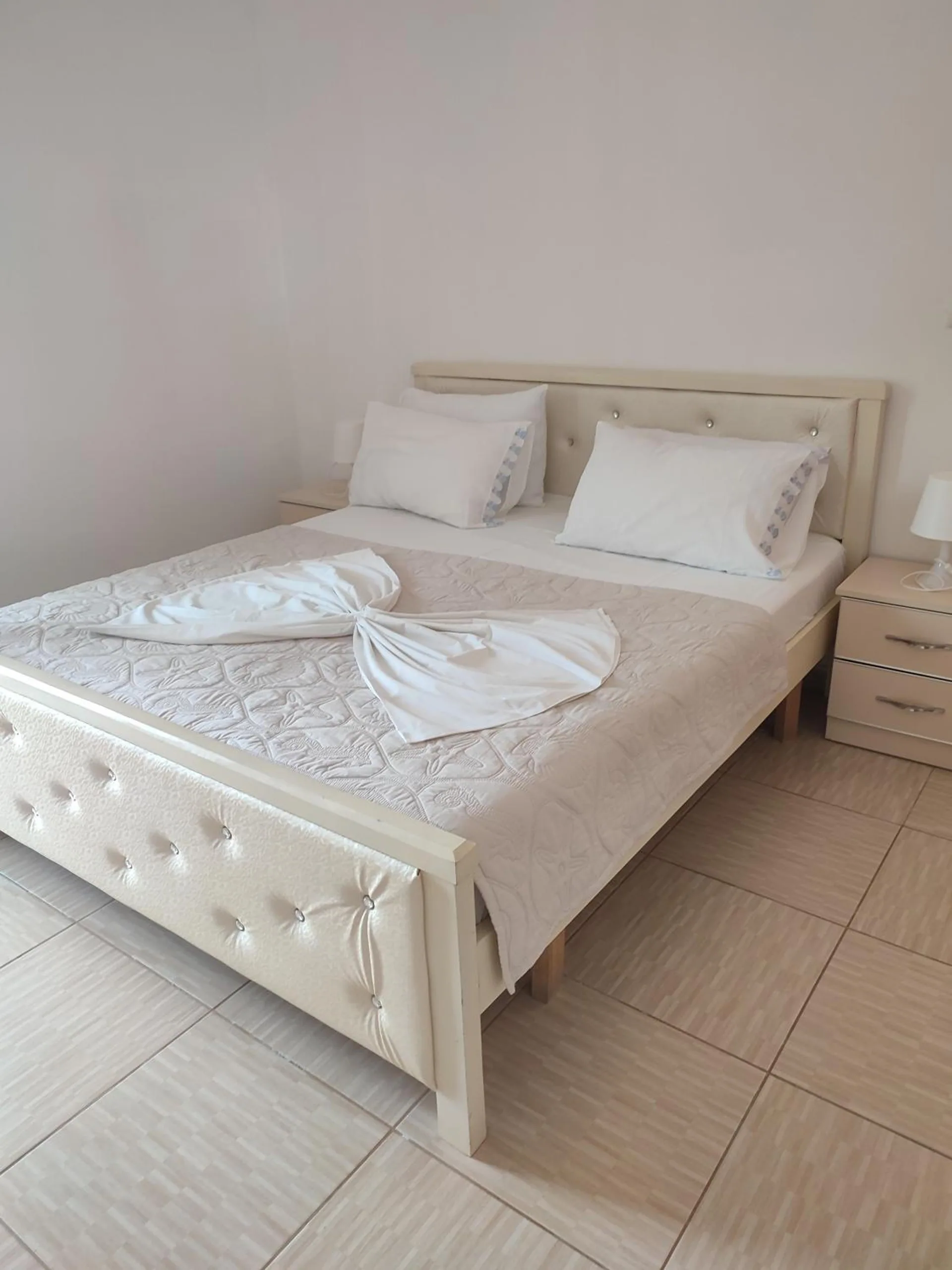 A double bed made up with white linen and towels, a bedside table beside it