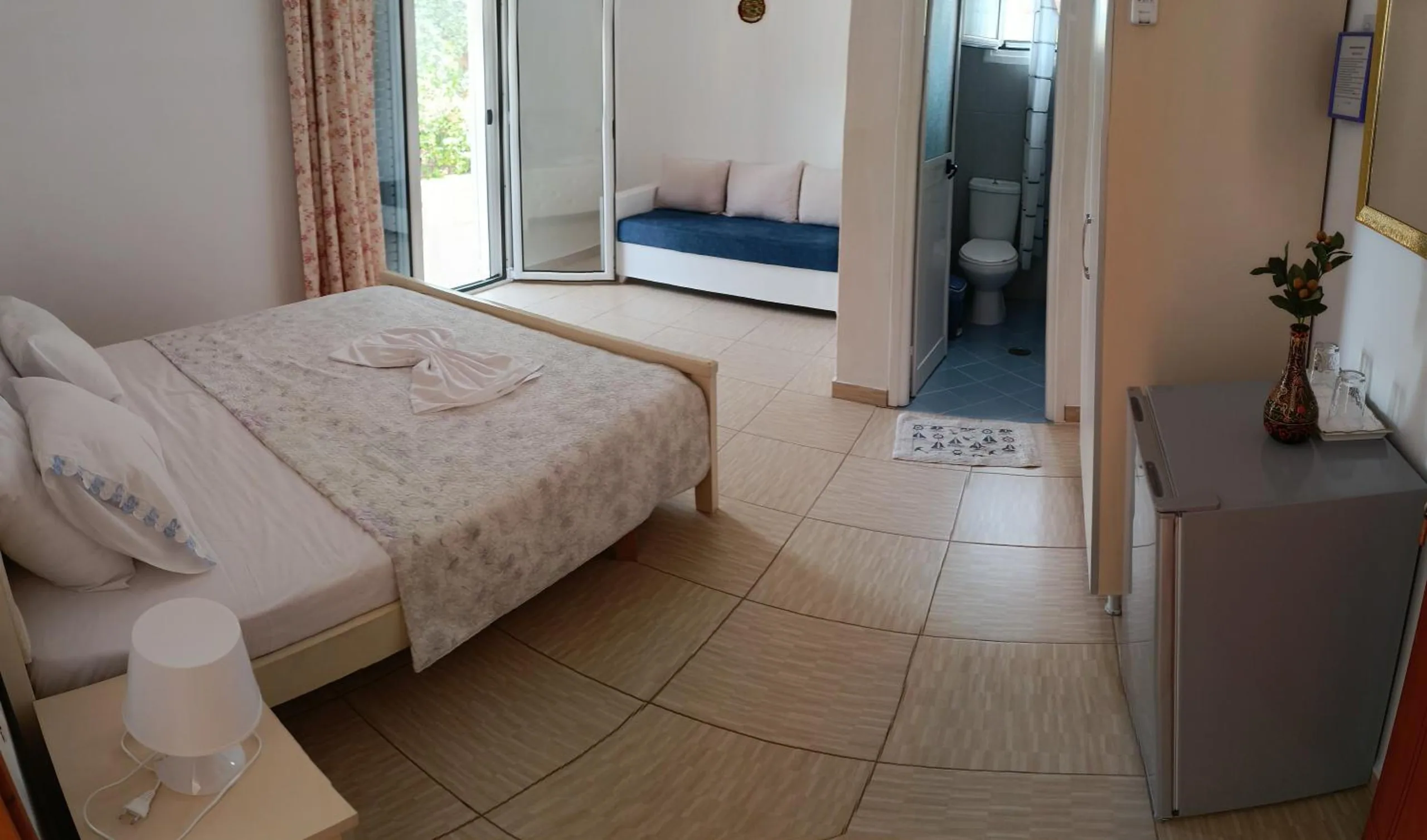 Wide view of a white room with a double bed, a daybed by the open balcony door and the shower room beyond