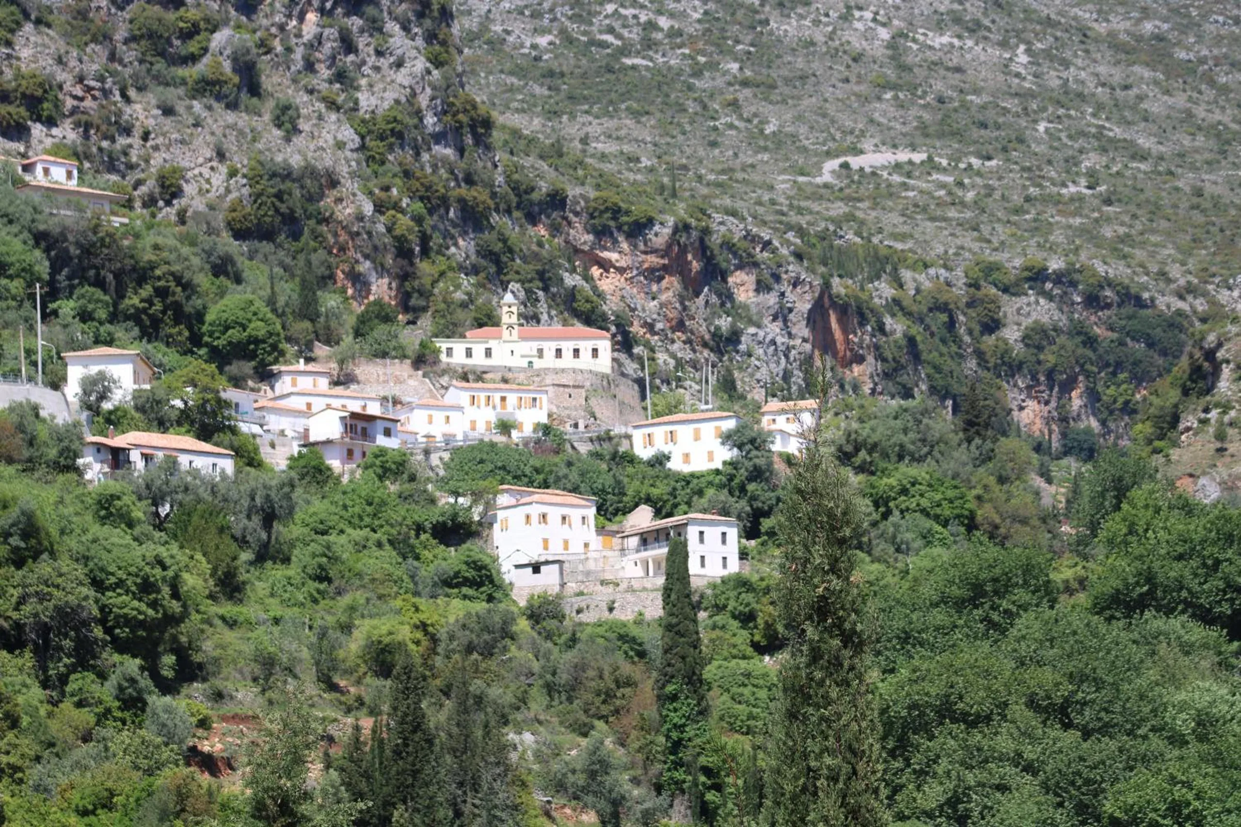 White stone houses of a village clustered on a steep green slope below grey cliffs