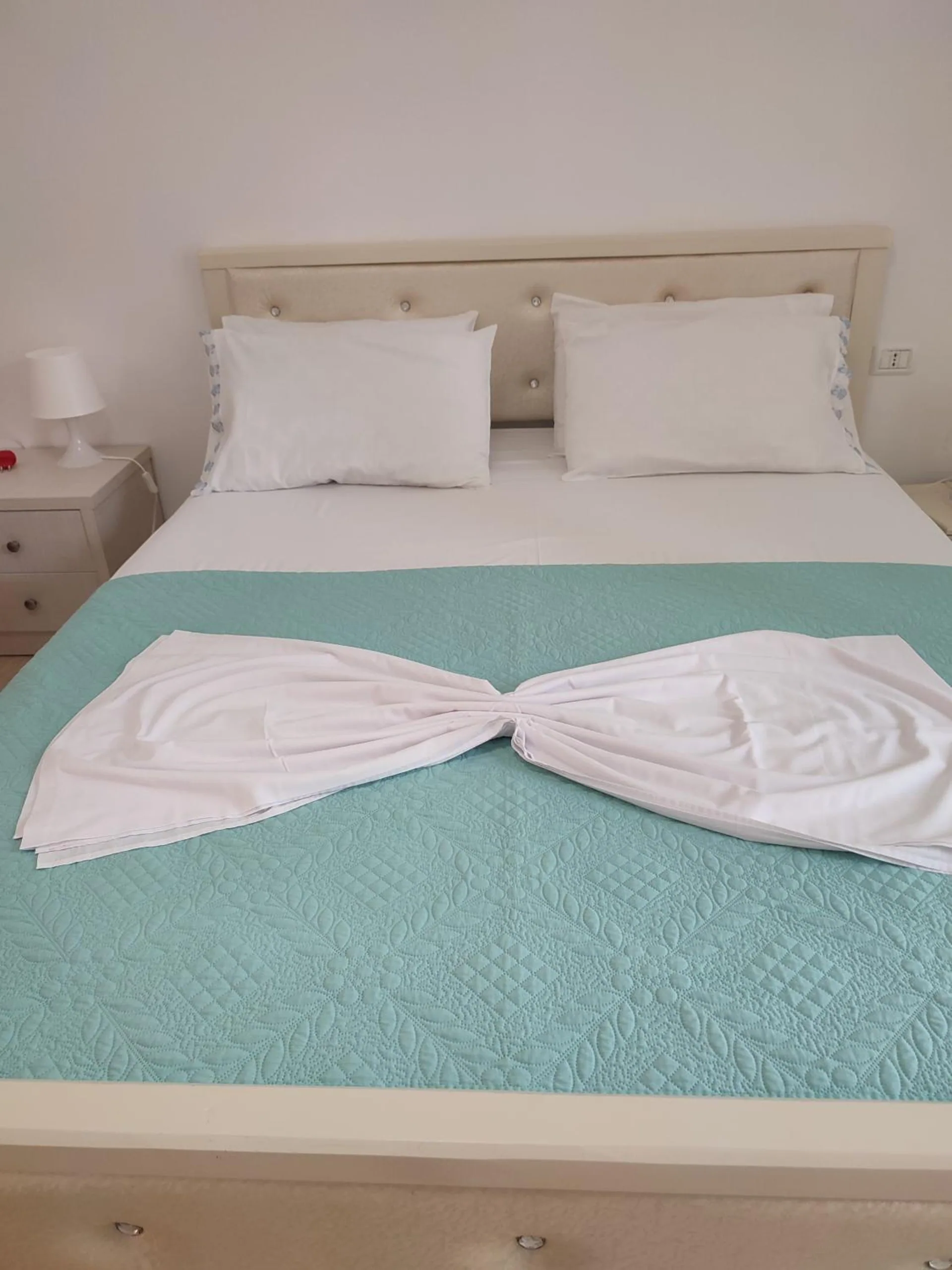 A double bed with a turquoise cover and white towels tied in a bow