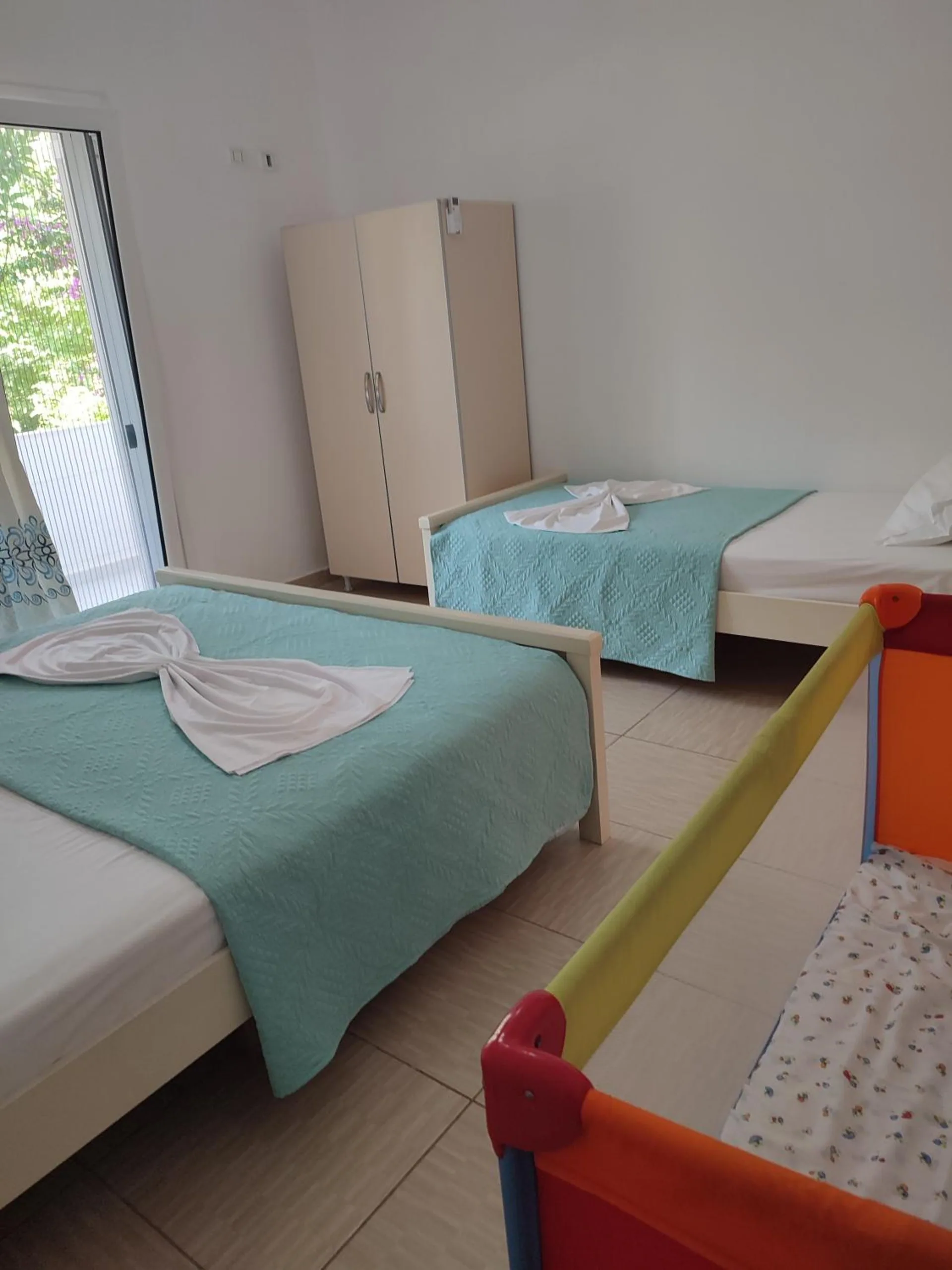 A family room with two beds under turquoise covers, a wardrobe and an orange travel cot