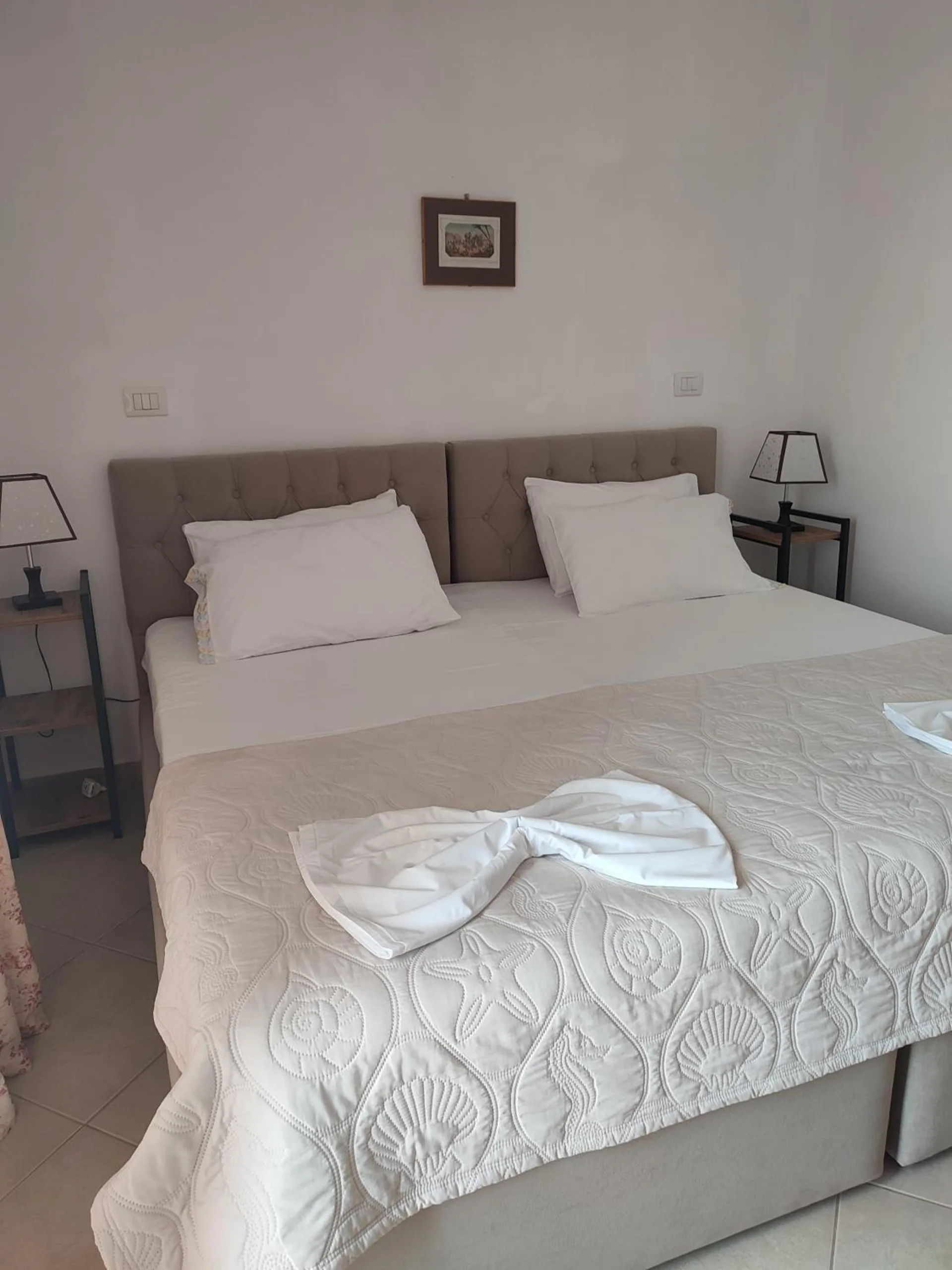 A double bed with an upholstered grey headboard and a white quilted cover, lamps either side