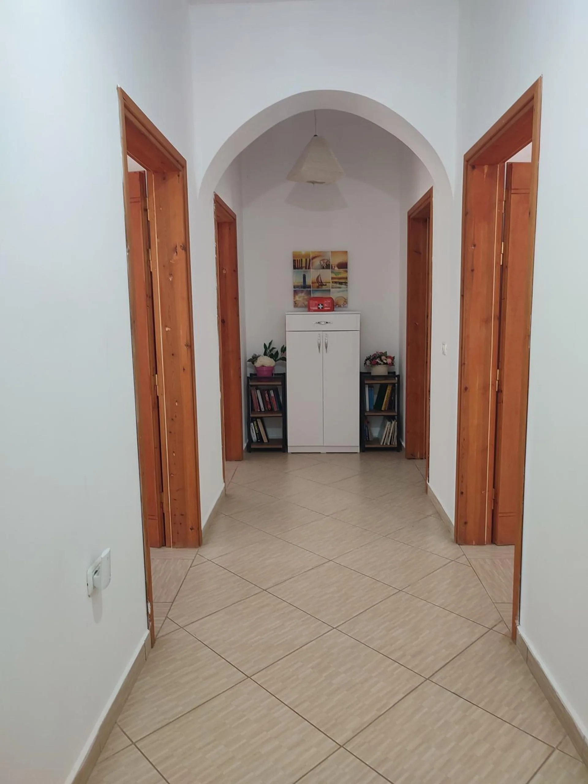 A white corridor with an arch, wooden doors on both sides and a tiled floor