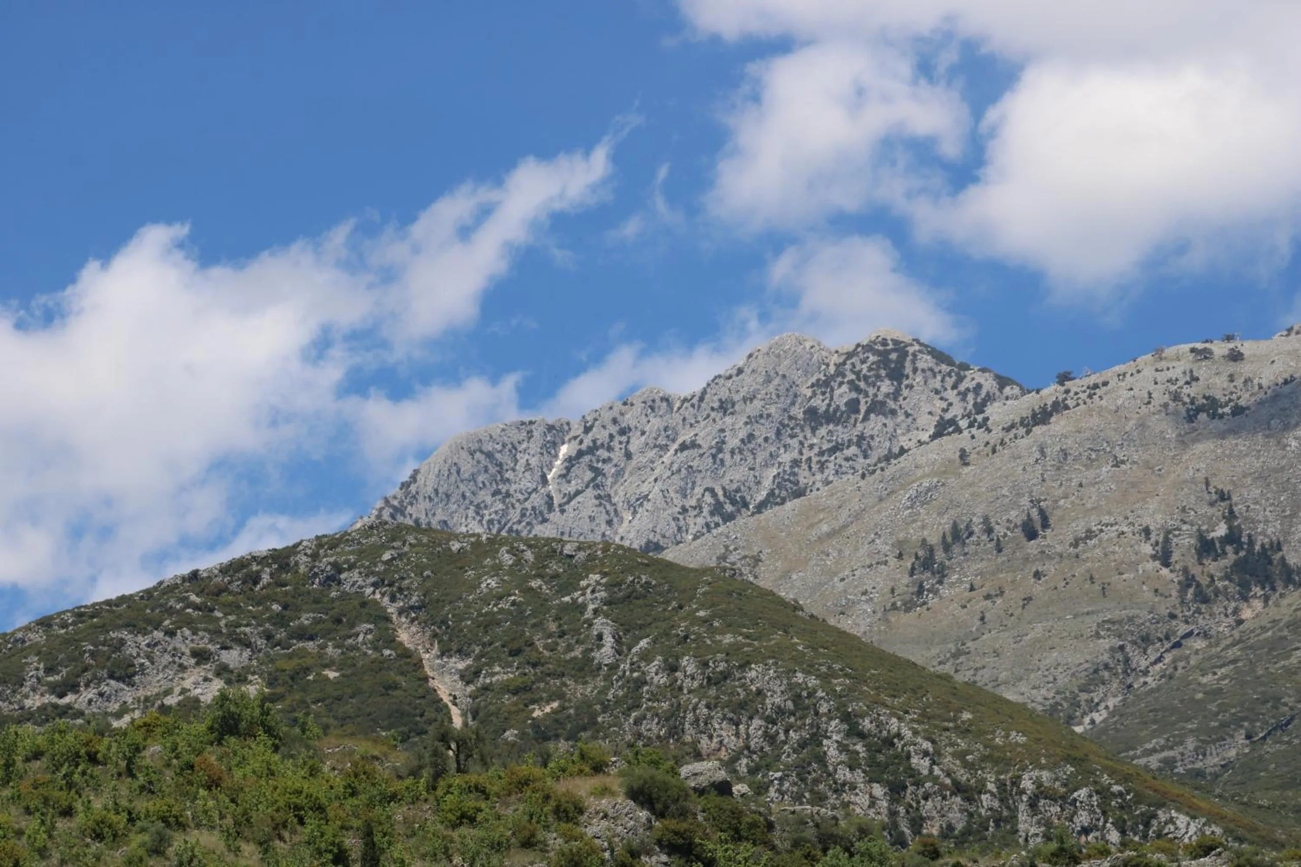 Grey limestone peaks over a green ridge under broken cloud
