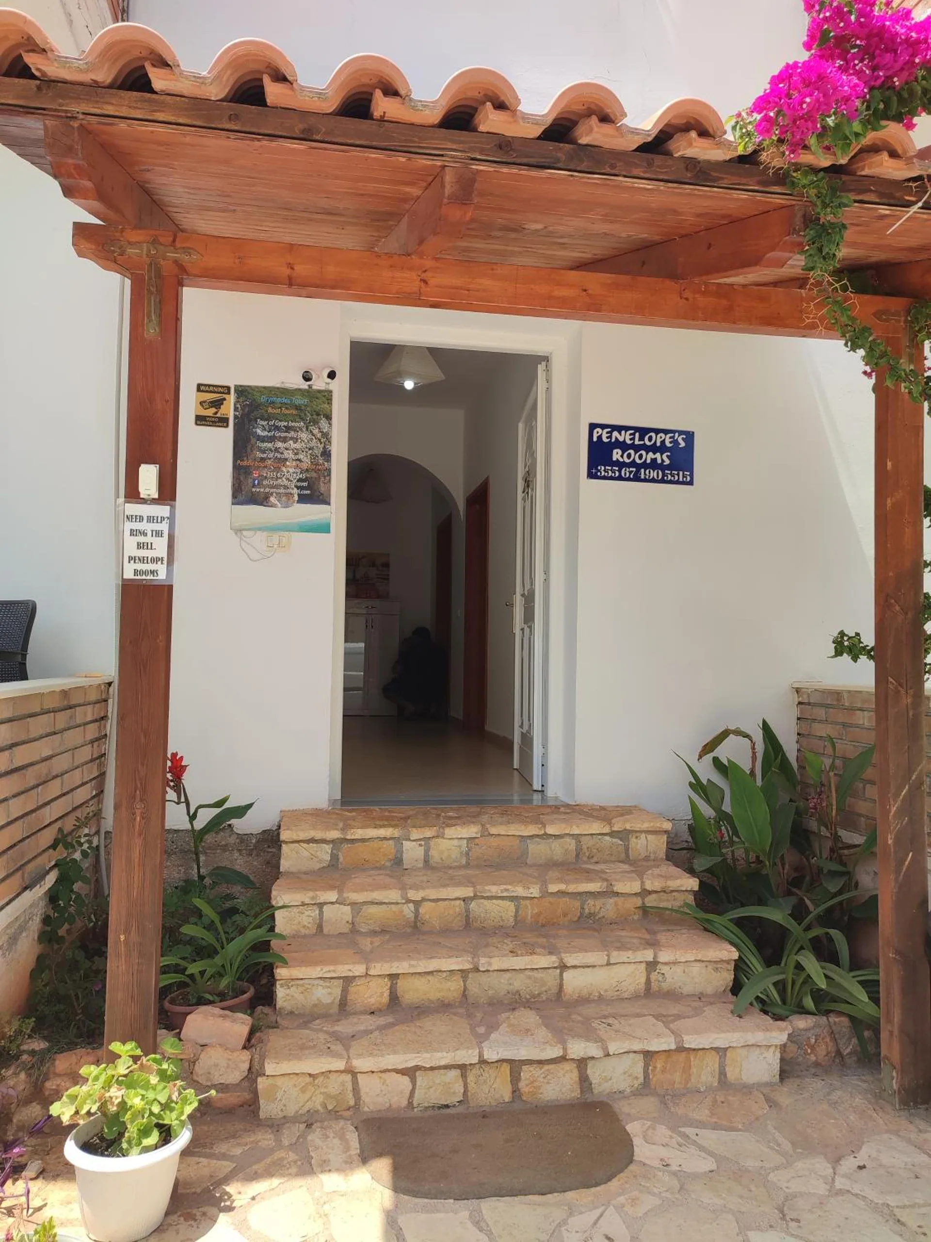 Stone steps up to the front door under a timber pergola with terracotta tiles, potted plants either side