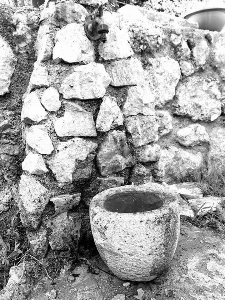 Black-and-white close-up of a stone mortar against a dry-stone wall
