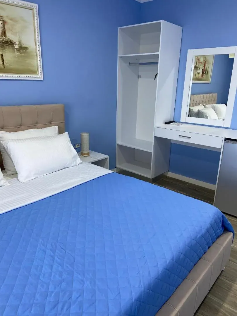 A blue room with an upholstered headboard, a blue bedspread, a desk and a mirror