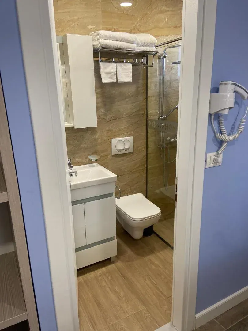 A bathroom with a basin, a wall-hung lavatory and a glazed shower lined in tan marble