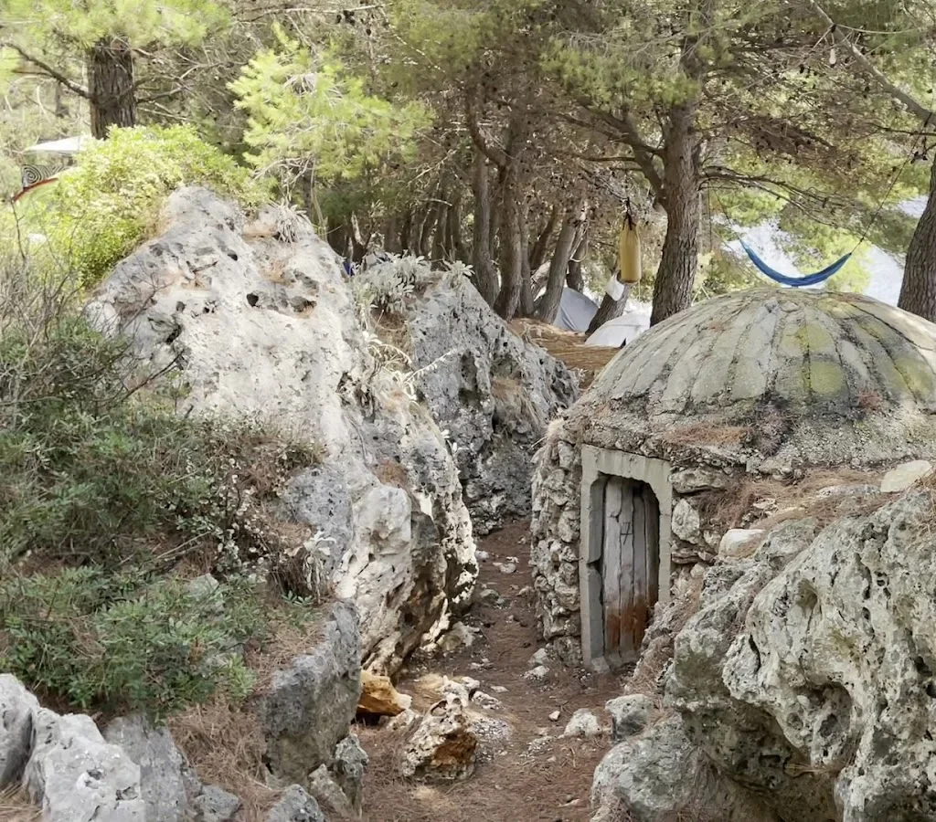 A concrete Hoxha-era dome bunker set into the limestone among pines at Pine Side Camp