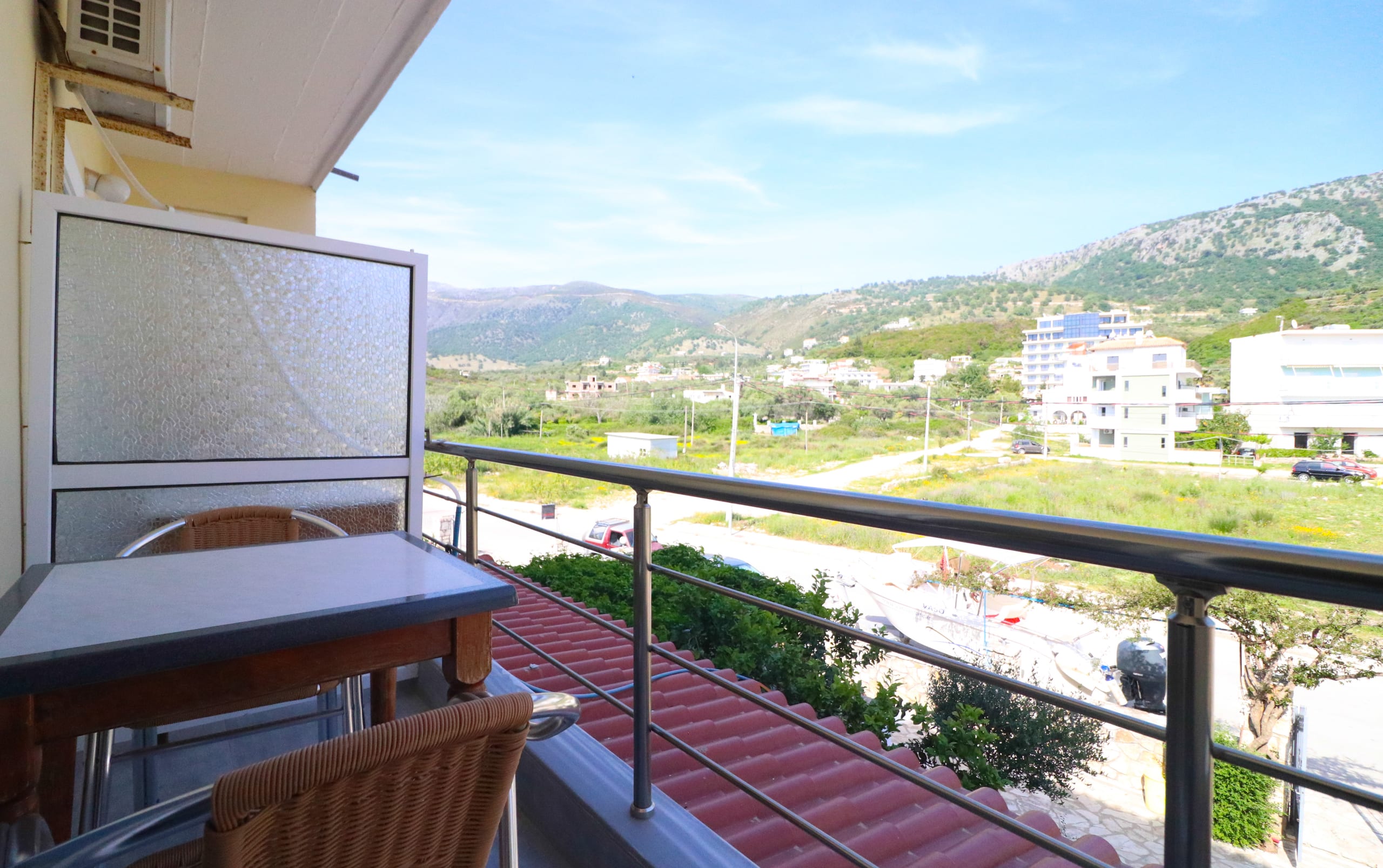 An upper balcony with a table and wicker chair looking inland over the coast road to the hills behind Potam