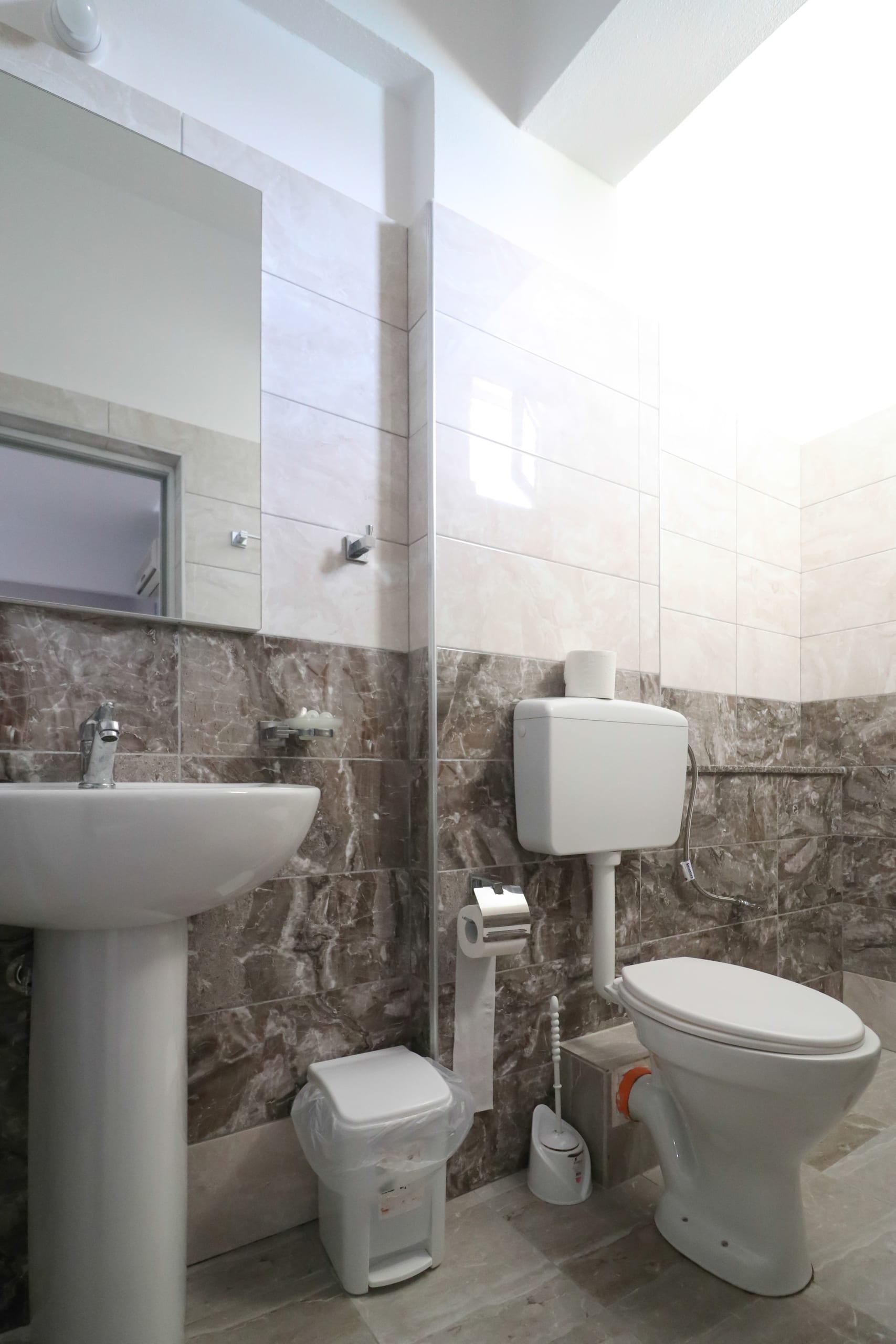 A bathroom with grey marble-effect tiles, a pedestal basin, a toilet and a frosted window