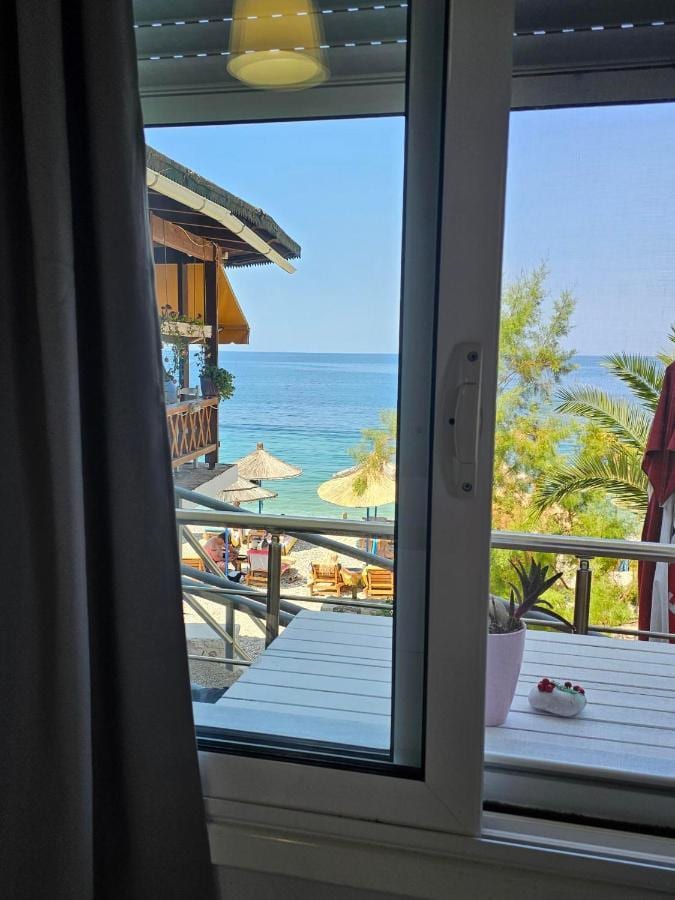 An open balcony door framing umbrellas on the beach and the blue sea beyond