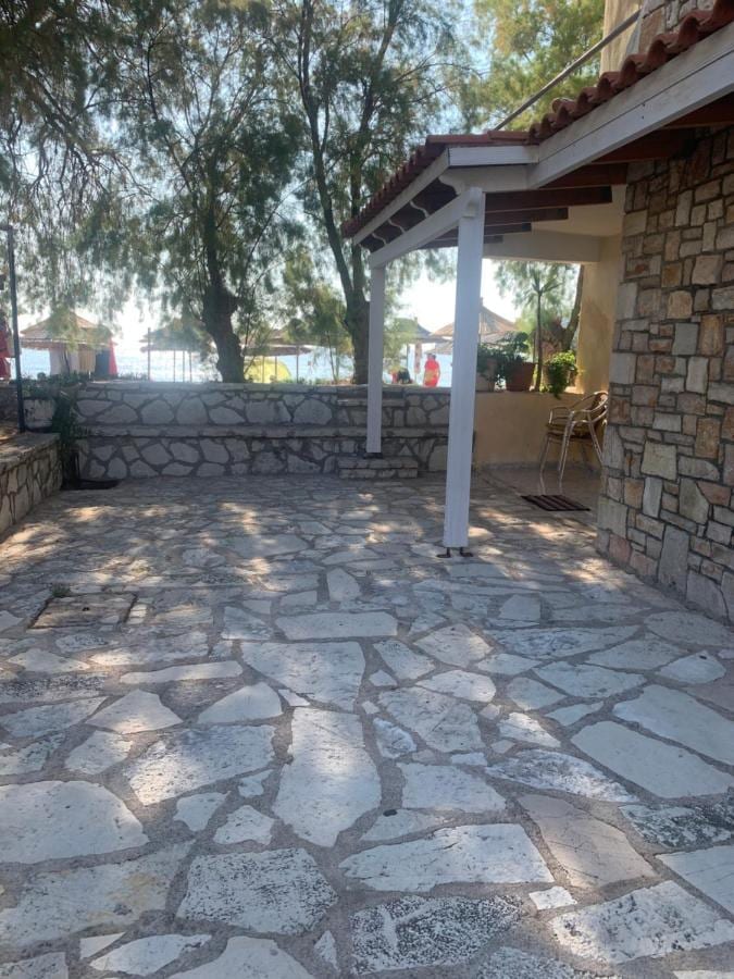 Dappled shade on a crazy-paved flagstone terrace with a stone wall and the beach umbrellas beyond
