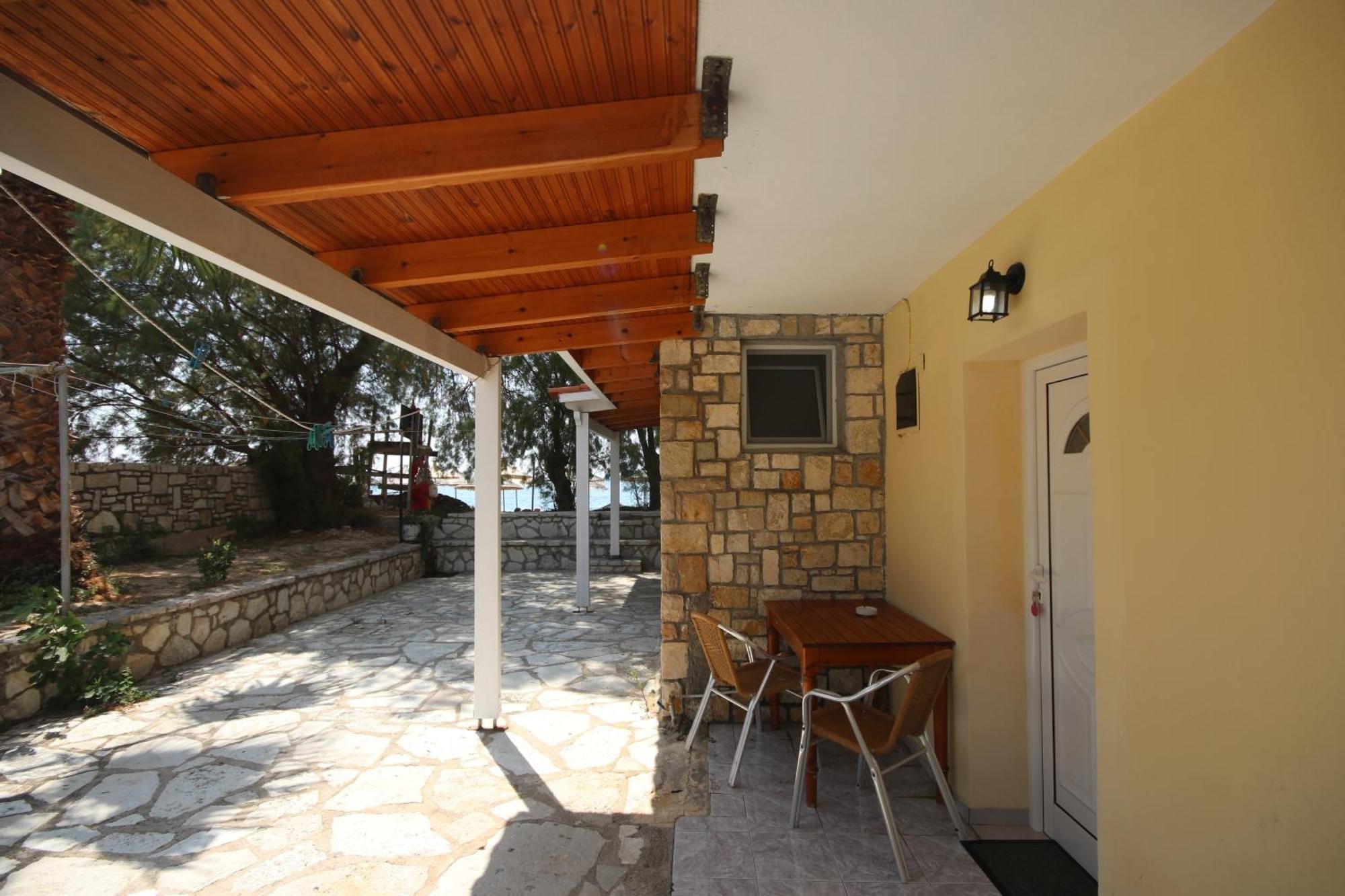 A ground-floor room door on a covered flagstone patio with a timber ceiling, a stone pier and a small table and chairs