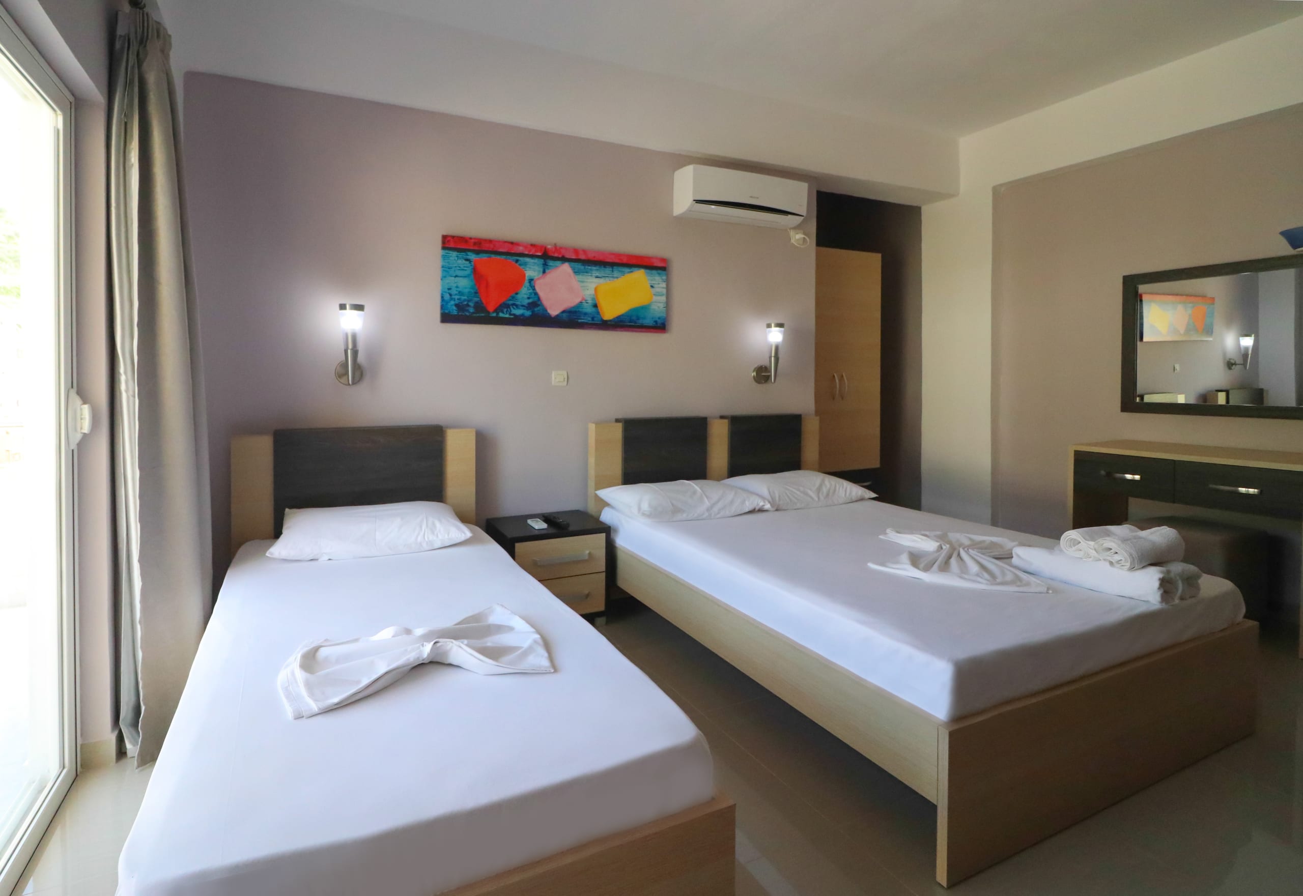 A room with a double bed and a single bed in pale oak, a bright painted canvas above them and an air conditioner on the wall