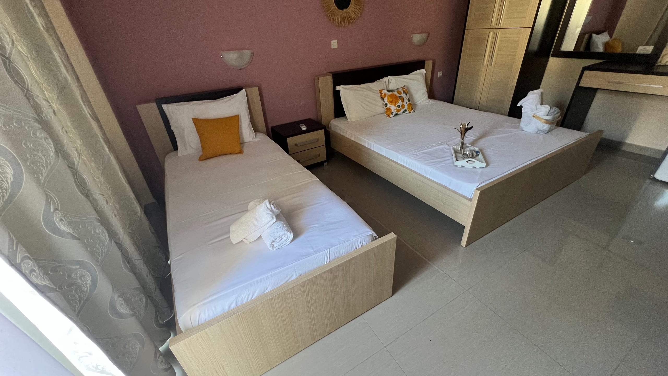 A room with a single and a double bed, a rose-coloured wall, wall lamps and an orange cushion