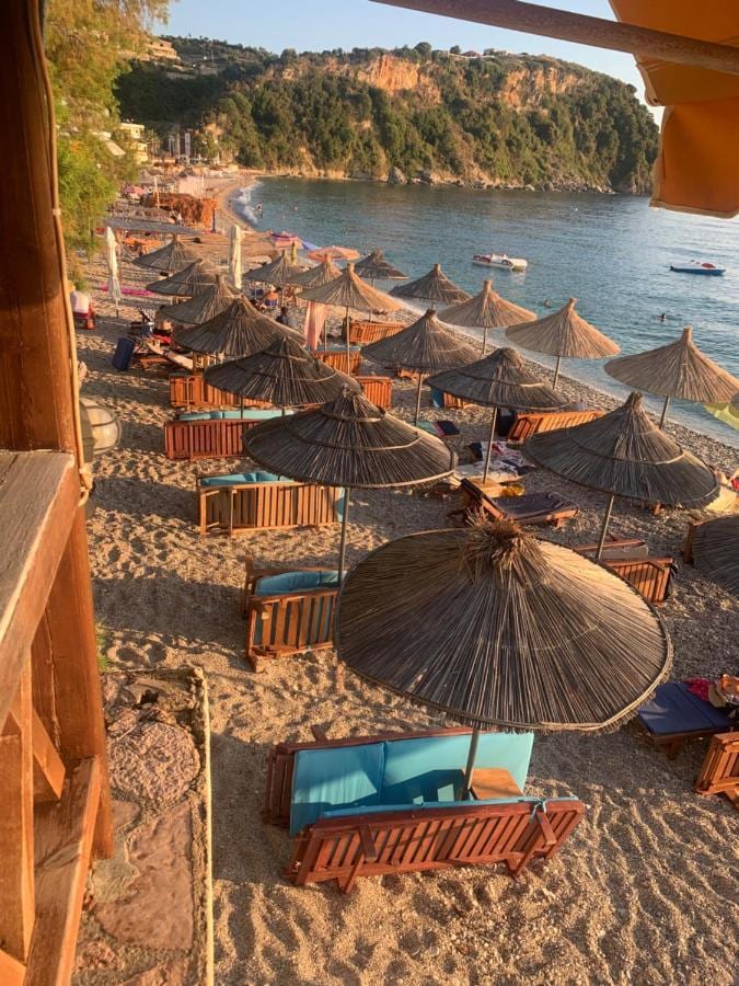 Thatched umbrellas and wooden sunbeds on the sand in the evening light, seen from the edge of the terrace