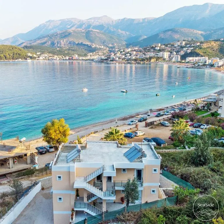 Potam bay from the hillside above Seaside Hotel: the hotel's roof and outside stair, the beachfront car park, the beach, and Himarë across the water