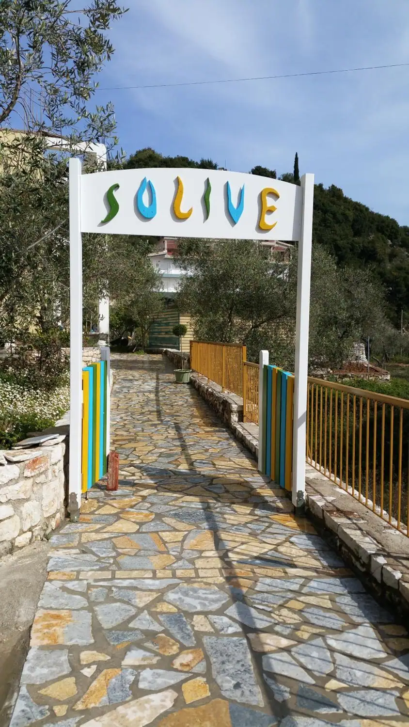 The white arch over the path into the guesthouse, with the name Solive in cut-out wooden letters painted green, blue and yellow, and a flagstone path running in under it