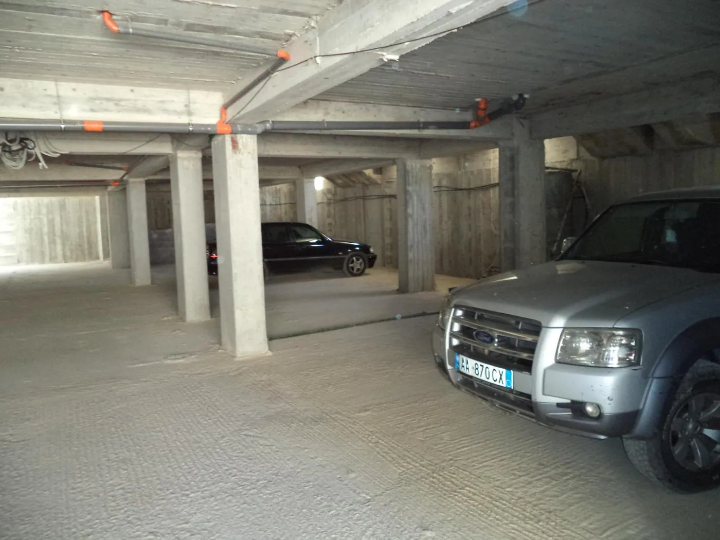 The covered parking garage under the house: a concrete floor and pillars with cars parked in bays