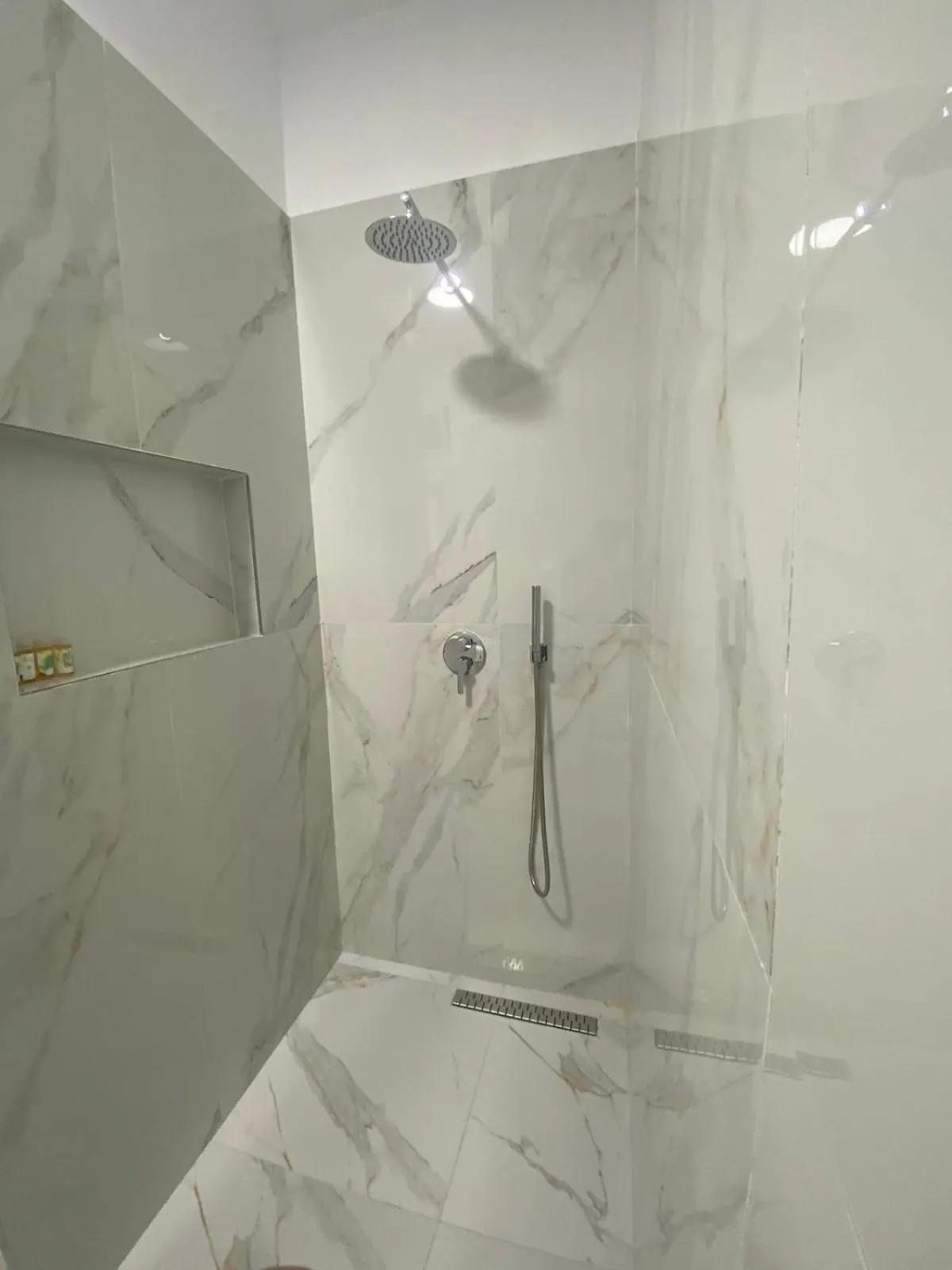 A walk-in shower behind a glass screen in white marble-effect tile