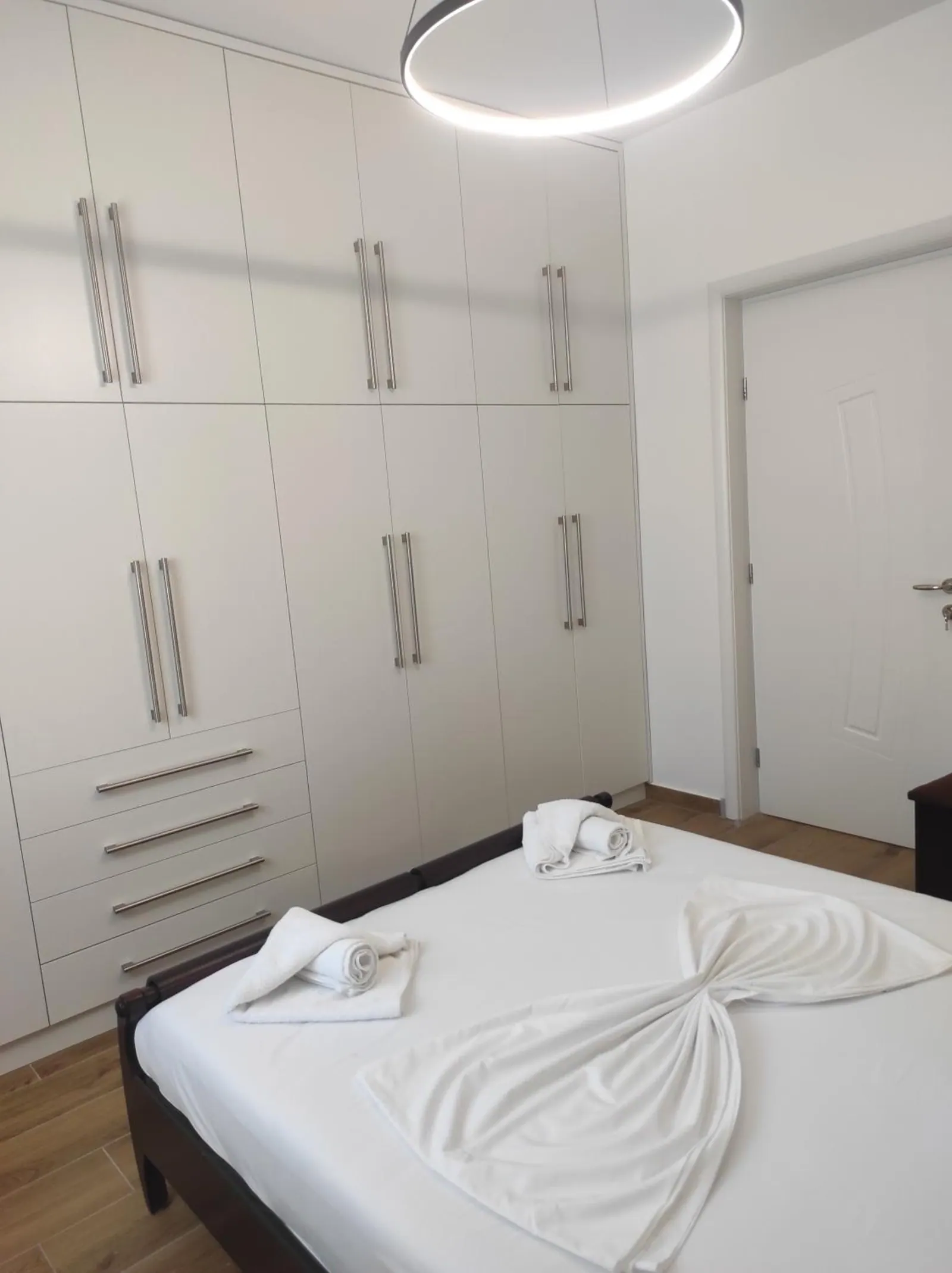 A wall of white built-in wardrobes and drawers above a double bed, a ring light overhead